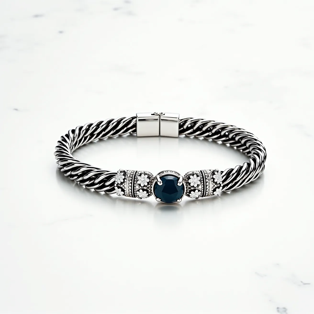 This men's bracelet features a stylish twisted cable design crafted from what appears to be stainless steel or a similar metal, enhancing its durability and modern aesthetic. The central element showcases a striking round-cut dark blue gemstone, possibly sapphire or onyx, set in a prong setting to secure it firmly in place. Flanking the central stone are intricate beadwork and floral motifs incorporating small, clear accent stones that could be diamonds or zirconias, adding a touch of elegance and sophistication. The bracelet is equipped with a sleek, rectangular clasp mechanism, ensuring a secure and comfortable fit for the wearer.