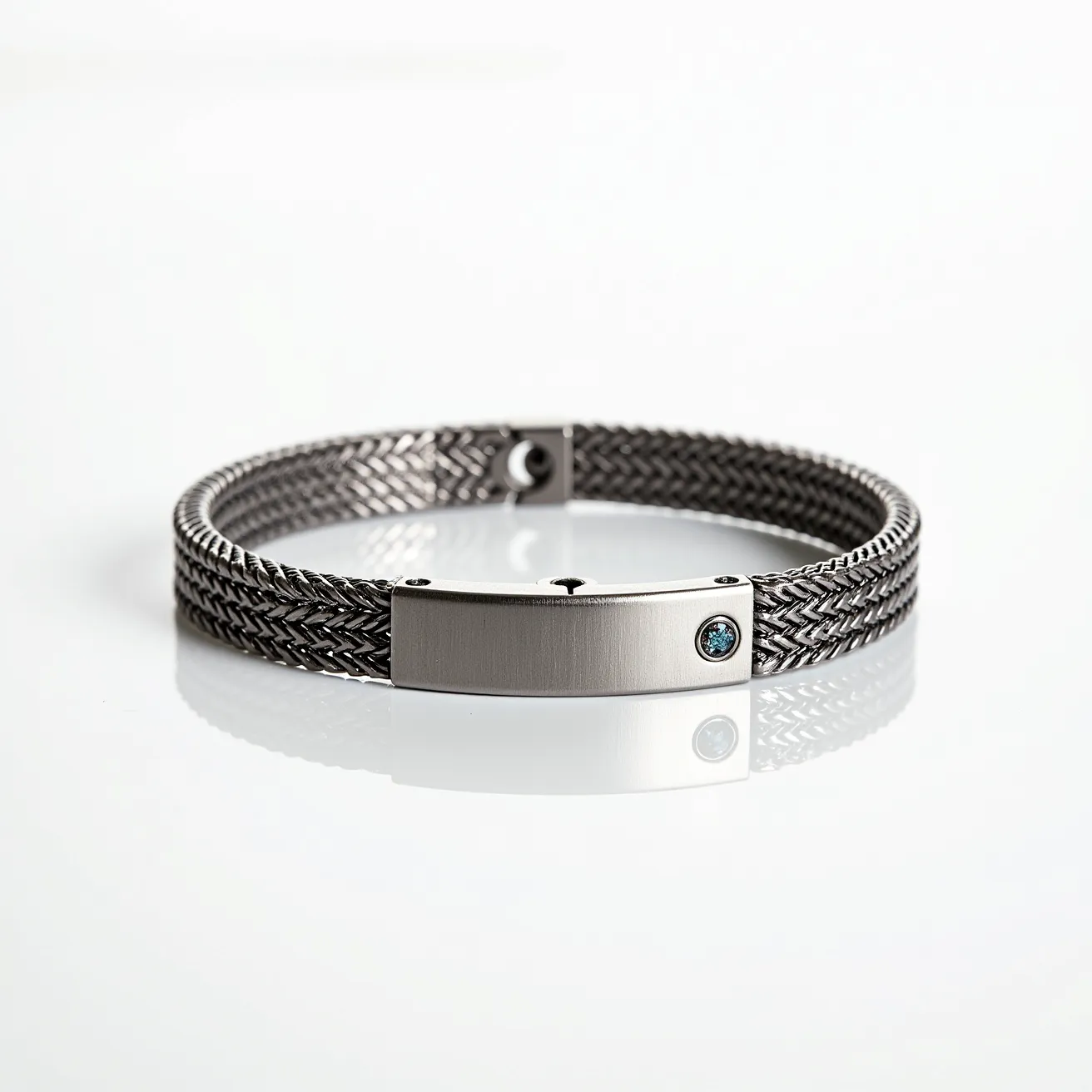 This men's bracelet showcases a sleek, woven design featuring a durable metal material, likely stainless steel, giving it a modern and sophisticated look. The bracelet is highlighted by a rectangular metal plate, functioning as both an aesthetic element and a central piece. Embedded within the metal plate is a small, round-cut gem, possibly a blue sapphire or a similarly colored stone, set securely, enhancing the bracelet's overall appeal. The clasp is integrated seamlessly into the design, ensuring a secure and stylish attachment when worn.