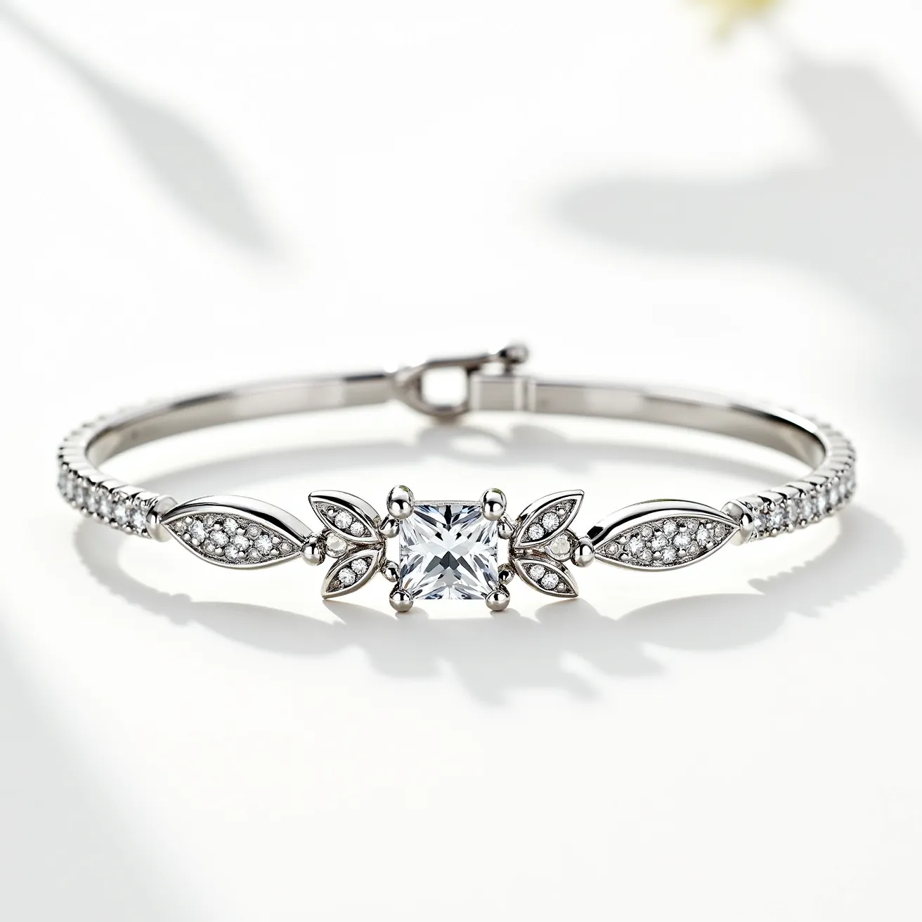 This moissanite tennis bracelet features a slender band adorned with small, round moissanite stones set in a continuous line, each held by four prongs. The centerpiece is a larger, square-cut moissanite stone, framed by a unique design of two marquise-shaped moissanite stones on either side, each accented with additional smaller round stones. The bracelet is crafted from a sleek, reflective metal, likely white gold or platinum, complementing the brilliance of the moissanite stones. The clasp is a secure, classic lobster-style clasp, providing both functionality and a sophisticated aesthetic.