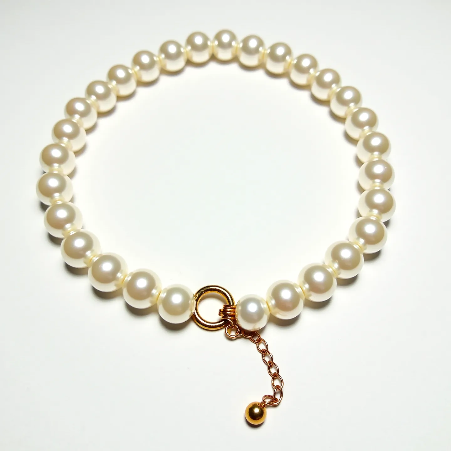 This pearl bracelet beautifully showcases a series of perfectly round, lustrous white pearls, each uniformly strung together to create an elegant and classic piece of jewelry. The pearls are likely cultured, given their consistent size and flawless appearance. Enhancing its sophistication, the bracelet features a gold-toned clasp attached to a delicate chain, detailed with a small, spherical bead at its end. The clasp, which appears to be a spring-ring mechanism, ensures a secure and easy fastening of the bracelet around the wrist, combining practicality with refined aesthetic appeal.