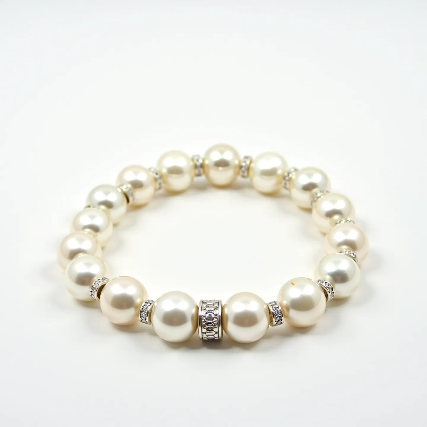 This pearl bracelet features a series of uniformly round and lustrous white pearls, each separated by small, clear, faceted gem spacers that add a touch of sparkle. The pearls appear to be meticulously matched in size, contributing to a balanced and elegant appearance. The centerpiece of the bracelet includes a larger, more ornate silver setting adorned with intricate detailing and encrusted with small, clear stones, providing a focal point of interest. The bracelet is designed without a traditional clasp, indicating it may be a stretch or elastic style for ease of wear.