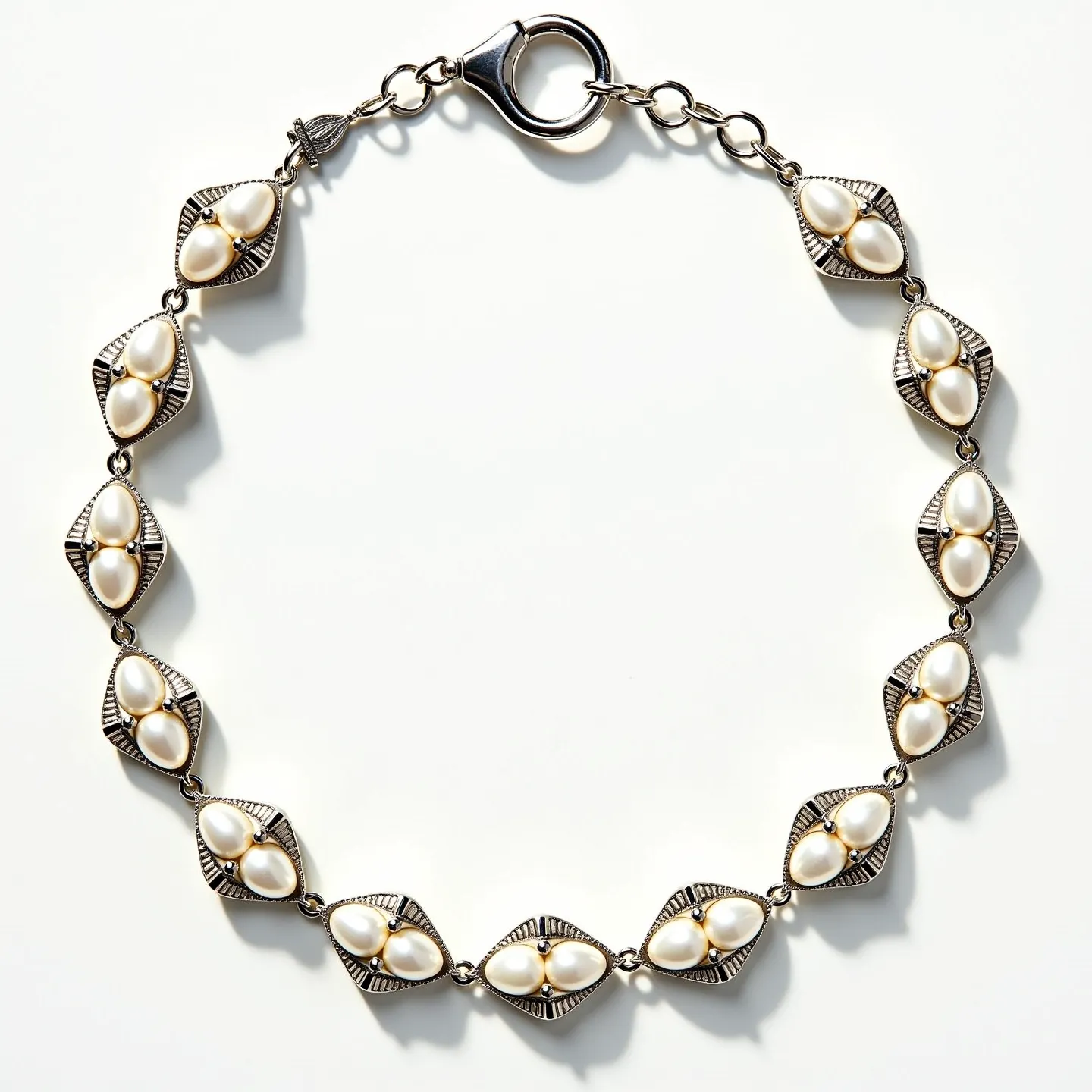 This pearl bracelet features a sequence of elegant, pearlescent oval pearls nestled in intricately designed, silver-toned metal settings. The pearls are arranged in pairs within each setting, creating a cluster that is both classic and refined. Each section is linked by small, circular connectors that contribute to the bracelet's fluidity and flexibility. The bracelet is secured with a lobster clasp, providing a sturdy and reliable closure. The interplay between the lustrous pearls and the detailed metalwork highlights the artisanship of this exquisite piece.