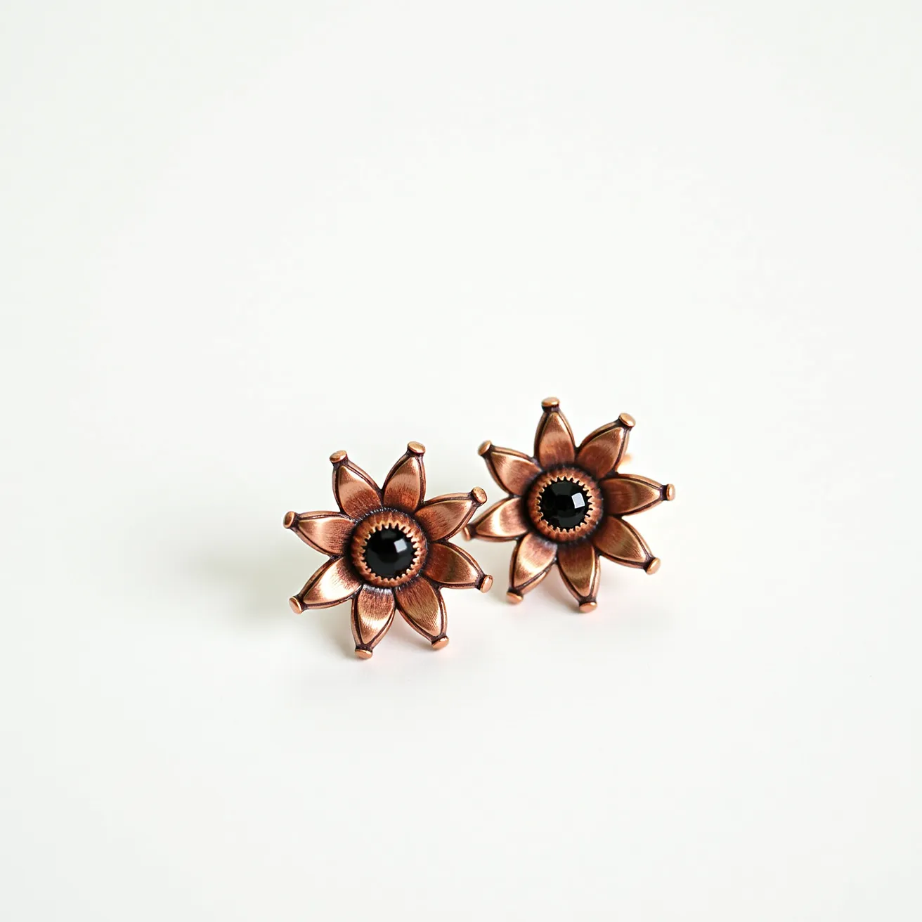 These 70s earrings feature a bold floral design crafted from a warm-toned metal, likely copper, which is common in vintage jewelry from that era. Each earring showcases a central black gemstone, which seems to be a faceted onyx, set in a round bezel that adds a classic touch. The petals of the flower are meticulously detailed, and the earrings are designed with a post-back attachment, making them secure and easy to wear. The combination of materials and design elements epitomizes the fashion-forward aesthetic of the 1970s.