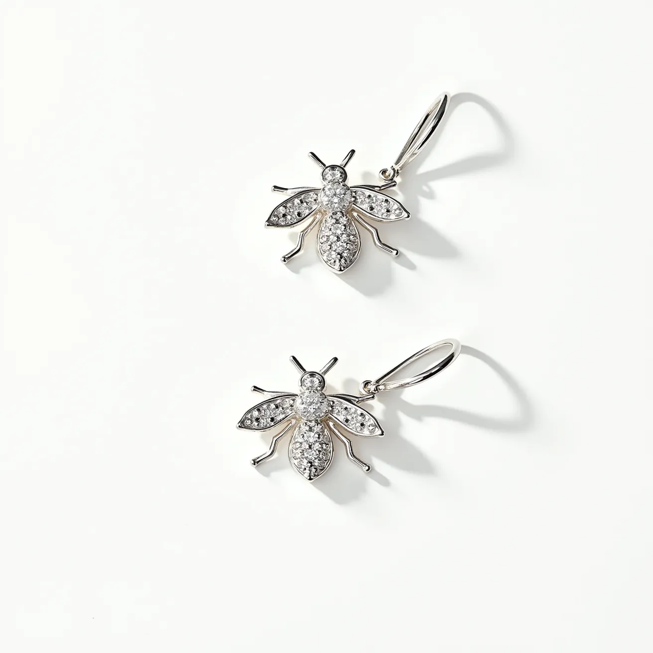 These bee earrings are crafted from a shiny silver-toned material, featuring intricate designs that mimic the form of bees. They are embellished with small, sparkling gems, possibly diamonds or cubic zirconia, set in a pavé style across the wings and body, adding a luxurious touch. The earrings attach via a classic hook clasp, which allows them to dangle elegantly. These details combine to create a charming accessory with a hint of whimsy and elegance.