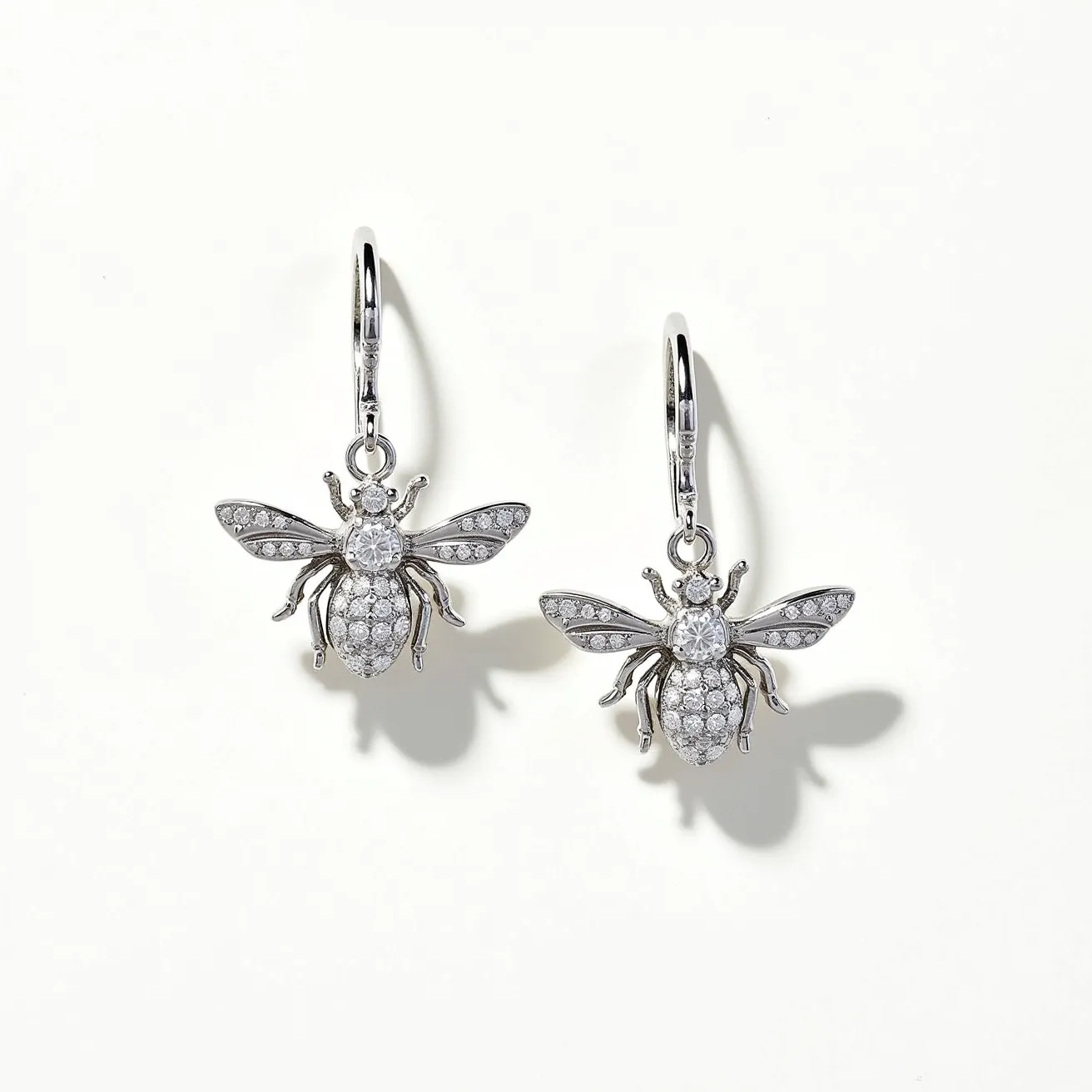 These bee earrings are crafted from a metallic material with a silver-toned finish, forming a detailed bee motif. The body and wings are encrusted with small, round-cut clear stones, likely cubic zirconia or diamonds, adding a touch of sparkle. These stones are set in a pavé style, enhancing the intricate design and the reflective quality of the earrings. The attachment features a lever-back clasp, providing both security and elegance for comfortable wear.