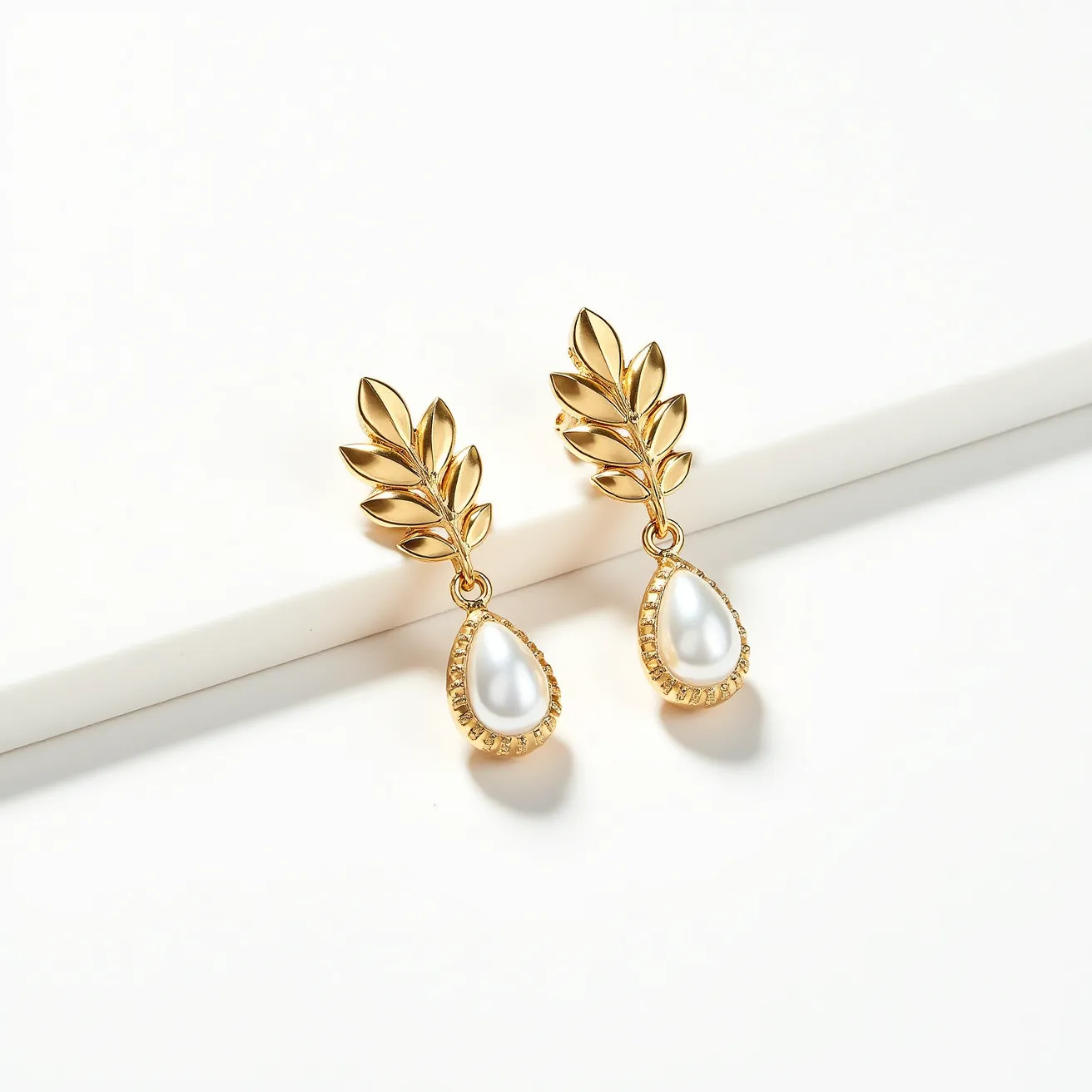 These birthstone earrings feature an elegant design with a delicate combination of materials and craftsmanship. The earrings show off a beautiful pear-shaped white gemstone, which could be a pearl or similar stone, set in a textured gold-tone bezel setting. Above the gemstone, there is a charming motif of gold leaves which lends a natural elegance to the design. The attachment appears to be a post or stud style, ensuring secure and comfortable wear while complementing the sophisticated aesthetic of the earrings.