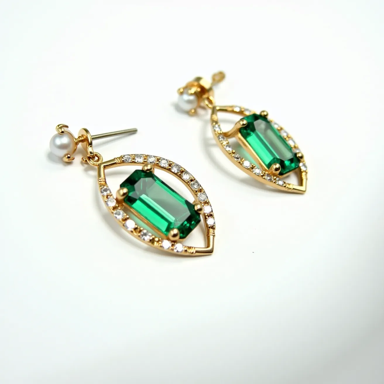 These birthstone earrings feature a stunning emerald-cut green gemstone as the centerpiece, likely representing the May birthstone, emerald. The gem is securely set within a gold-toned, marquise-shaped setting adorned with a halo of small, round, clear stones, possibly diamonds or cubic zirconia, enhancing its brilliance. Attached to each earring is a lustrous pearl, adding a classic touch to the elegant design. These earrings utilize a post-and-butterfly clasp for secure and comfortable wear, beautifully combining elegance with the rich symbolism of birthstones.