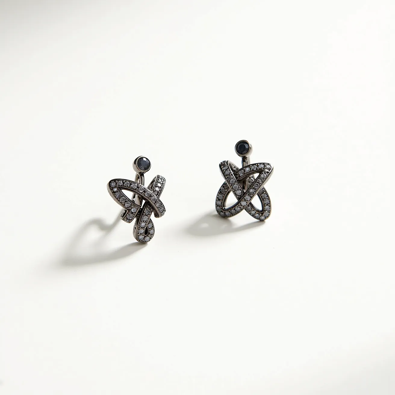 These black earrings are composed of intricately designed metal, featuring a layered knot-like pattern adorned with small, round, clear stones set closely together. At the top of each earring is a single, larger dark stone, possibly an onyx or black diamond, set in a simple bezel setting that complements the overall design. The earrings likely have a post-back clasp for secure attachment, offering both elegance and stability. The combination of the shiny dark stones and the sparkling clear gems provides a striking contrast, enhancing the luxurious and sophisticated appearance of the earrings.