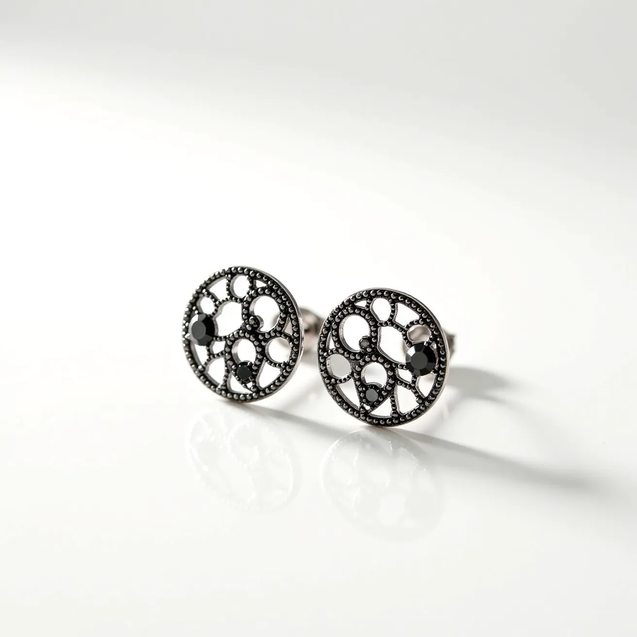 These black earrings feature a sophisticated design with circular elements forming an intricate lace-like pattern. The earrings are crafted from a dark metallic material, possibly a blackened silver or similar base metal, adding depth and elegance to their appearance. Embedded within the design are several small, faceted black stones that could be black diamonds or onyx, adding a touch of sparkle. The stones are securely set in a prong setting, integrating seamlessly into the openwork design. These earrings include a post and butterfly clasp, ensuring a secure and comfortable fit.