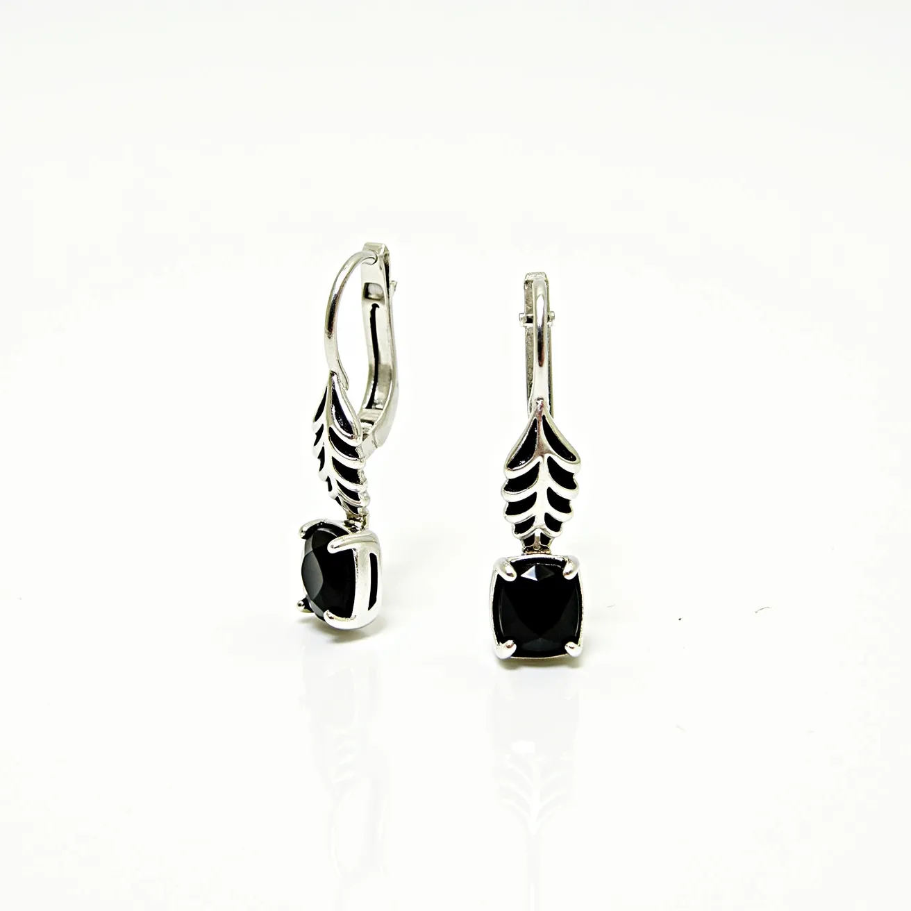 These black earrings feature a sophisticated design with prominent square-cut black gemstones, possibly onyx or black spinel, set securely in a four-prong setting. The stones are elegantly complemented by a stylized silver or platinum metal design, which resembles an intricate, leaf-like pattern, adding a touch of elegance and uniqueness to the earrings. The clasp is a classic lever-back style, ensuring a secure and comfortable fit when worn. The combination of the dark gemstones and the bright metal creates a striking contrast, making these earrings a versatile accessory for various occasions.