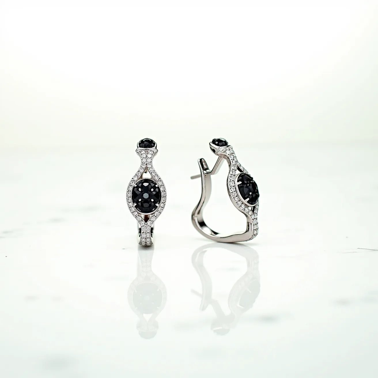 These black earrings feature a sophisticated design with a central black stone, possibly onyx or a black diamond, cut in an oval shape and beautifully set in an intricate bezel setting. Surrounding the main stone is an array of small, clear stones, likely diamonds, which add a touch of sparkle and contrast against the black centerpiece. The earrings are crafted from a shiny metal, possibly white gold or silver, enhancing their elegant appearance. The hoop style includes a secure hinged clasp, ensuring they stay firmly in place when worn. Their refined design makes these earrings a perfect accessory for both formal occasions and stylish everyday wear.