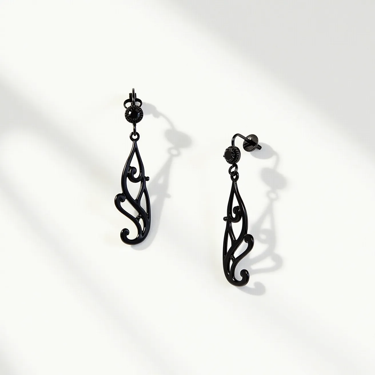 These black earrings feature an elegant and intricate design with a filigree pattern. The material appears to be a dark, possibly oxidized or blackened metal, which gives it a sleek and contemporary look. At the top of each earring, there is a small, round gem, which looks like it could be a black diamond or a similarly dark stone, set in a bezel setting to enhance its sophisticated appeal. The earrings are designed with hook or lever-back clasps, providing a secure and comfortable fit for the wearer. The overall craftsmanship highlights an artistic flair, making these earrings a stylish accessory for various occasions.