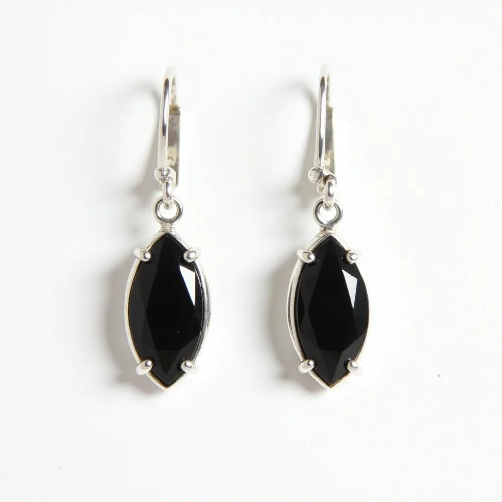 These black earrings feature a striking marquise-shaped black gemstone, likely onyx or a similar stone, which is elegantly faceted to catch the light. Each stone is secured with a classic four-prong setting, ensuring durability and a polished look. The metal surrounding and setting the stone appears to be silver, complementing the dark hue of the gems. These earrings are designed with leverback clasps, which provide a secure attachment while offering ease of wear. The overall design combines a modern aesthetic with timeless elegance, making them suitable for various occasions.