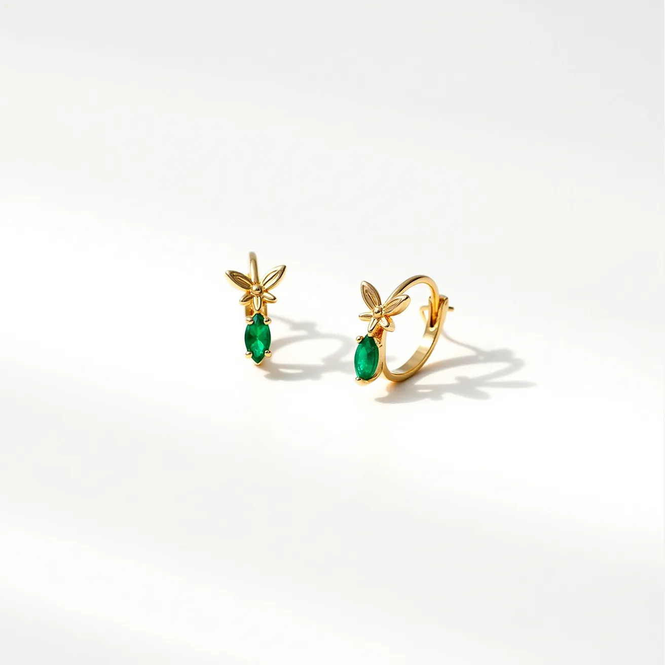 These cartilage hoop earrings are crafted from gold-toned metal, featuring a delicate design with a floral motif at the top. Each hoop is adorned with a single, vibrant green gemstone, likely an emerald, shaped in an oval cut and set with prongs to secure it in place. The earrings have a sleek, curved design that complements the attached floral element. For the clasp mechanism, they utilize a hinged or latch-back design, offering ease of wear while ensuring the hoops remain securely fastened on the ear. The overall look is elegant and refined, perfect for adding a touch of color and elegance to the ear.