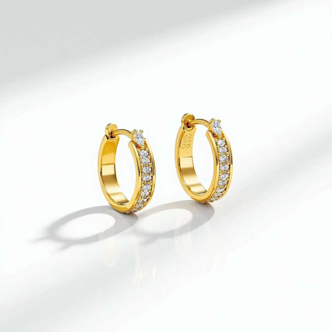 These cartilage hoop earrings are crafted in gold and feature a row of round-cut diamonds set along the outer curve, each held in place with prong settings. At the top of each hoop, there is a larger, marquise-cut diamond, adding a distinctive focal point to the design. The earrings are secured with a hinged clasp mechanism, ensuring a snug fit suitable for cartilage piercings. The combination of gold and diamonds creates an elegant and timeless look, perfect for adding a touch of sophistication.