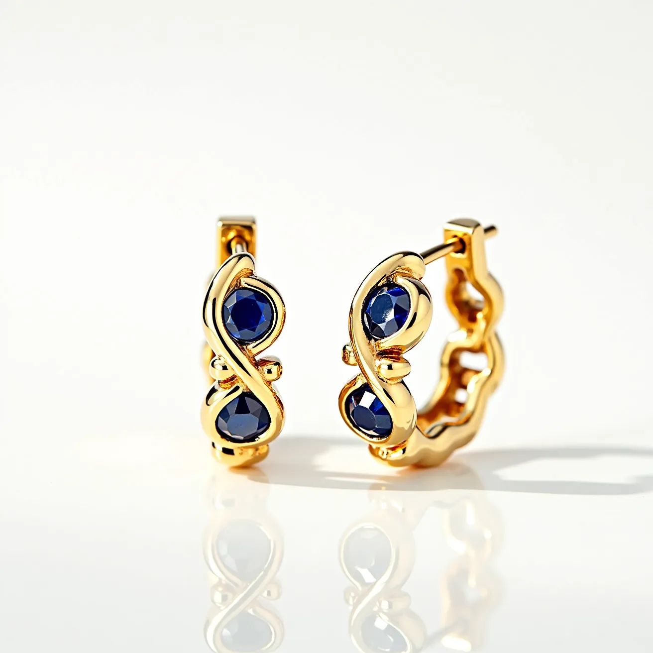 These cartilage hoop earrings are crafted from a lustrous gold material, exuding a luxurious and classic appeal. They feature deep blue stones, likely sapphires, cut into smooth rounds and securely nestled in a bezel setting which enhances their captivating hue. The design includes an intricate looped pattern that intertwines elegantly around the stones, providing a sophisticated and artistic flair. The hoops are equipped with a hinge closure that ensures a secure and comfortable fit when worn, making them both practical and stylish for everyday use.