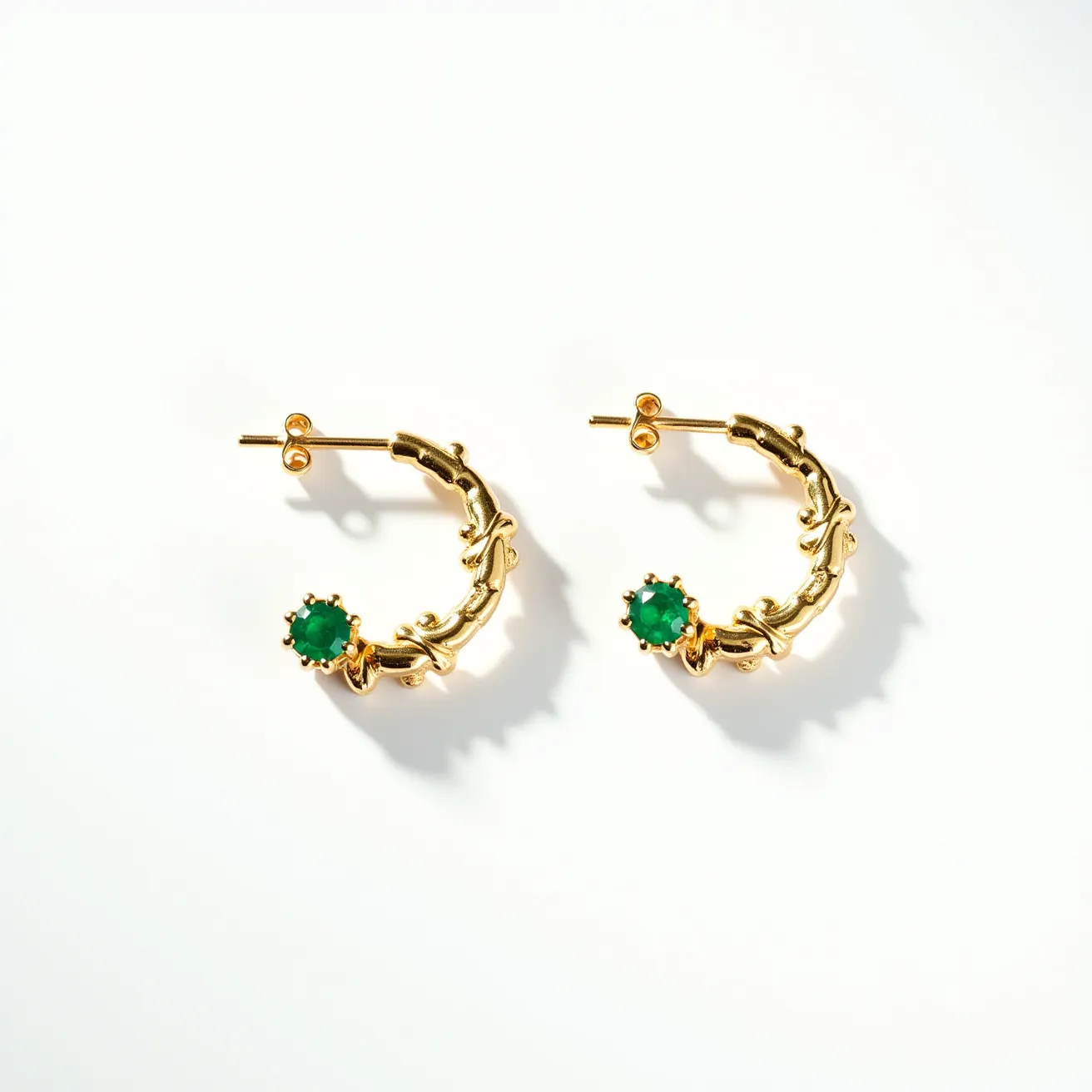 These cartilage hoop earrings are crafted from a gold-toned metal featuring an intricate leafy design along the hoop. They are adorned with round, faceted green gemstones set in a prong setting, adding a vibrant touch to the accessory. The earrings are secured with a classic post and butterfly clutch backing, ensuring a comfortable and secure fit. The combination of the rich gold hue and the deep green stones creates an elegant and eye-catching piece suitable for various occasions.