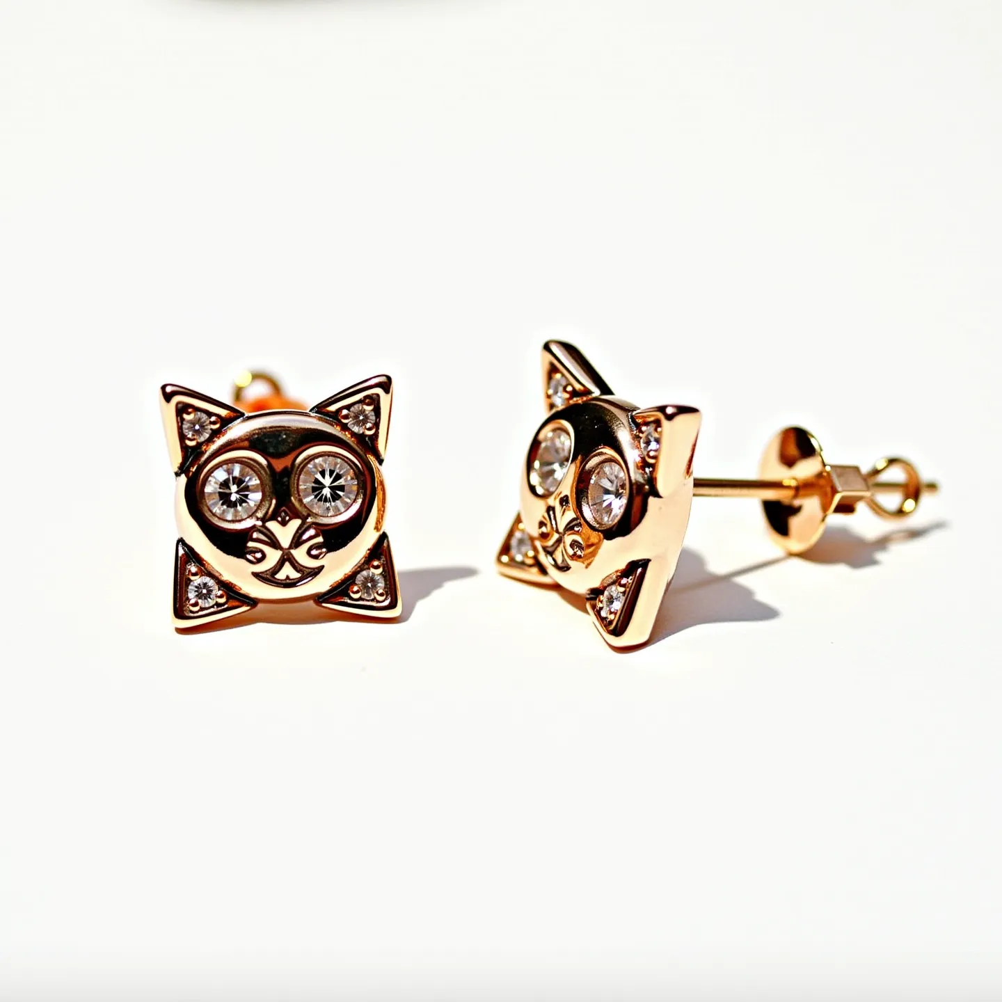 These cat earrings are crafted from a gold-toned metal, featuring a playful design that resembles a cat's face. The earrings showcase two prominent round, clear stones representing the cat's eyes, set in a secure bezel setting to enhance their sparkle. Additional smaller stones are embedded in the corners of the cat's ears, adding extra brilliance and detailing to the piece. The earrings are attached using a post and butterfly clutch back, ensuring a secure fit while worn. The combination of the playful cat motif with the elegant stone accents creates a charming and whimsical accessory.