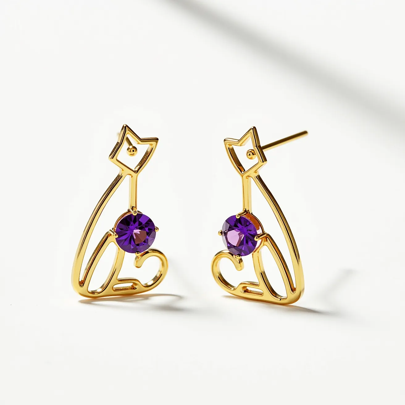 These cat earrings feature an elegant gold-toned metal crafted to depict a minimalist cat silhouette. The design incorporates a round, faceted purple gem that is centrally set using a prong setting, adding a touch of vibrancy to the piece. Each earring is equipped with a post-back attachment, providing a secure and comfortable fit for pierced ears. The combination of the gold metal and the striking purple gem creates a sophisticated and whimsical accessory.