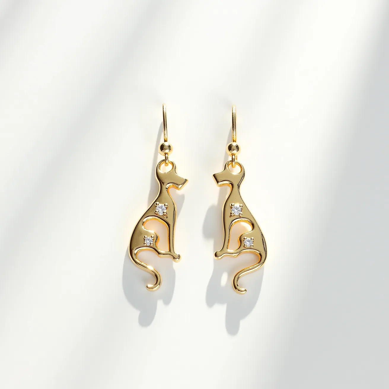 These cat earrings feature an elegant design crafted from a gold-toned metal, shaped into sleek silhouettes of sitting cats. Each earring is adorned with small, clear gemstones that add a touch of sparkle, possibly resembling diamonds set in a prong or bezel setting. The earrings are suspended from simple hooks, allowing for easy wear and a graceful dangle. The curves and minimalist design accentuate the feline form, creating a charming and sophisticated accessory.