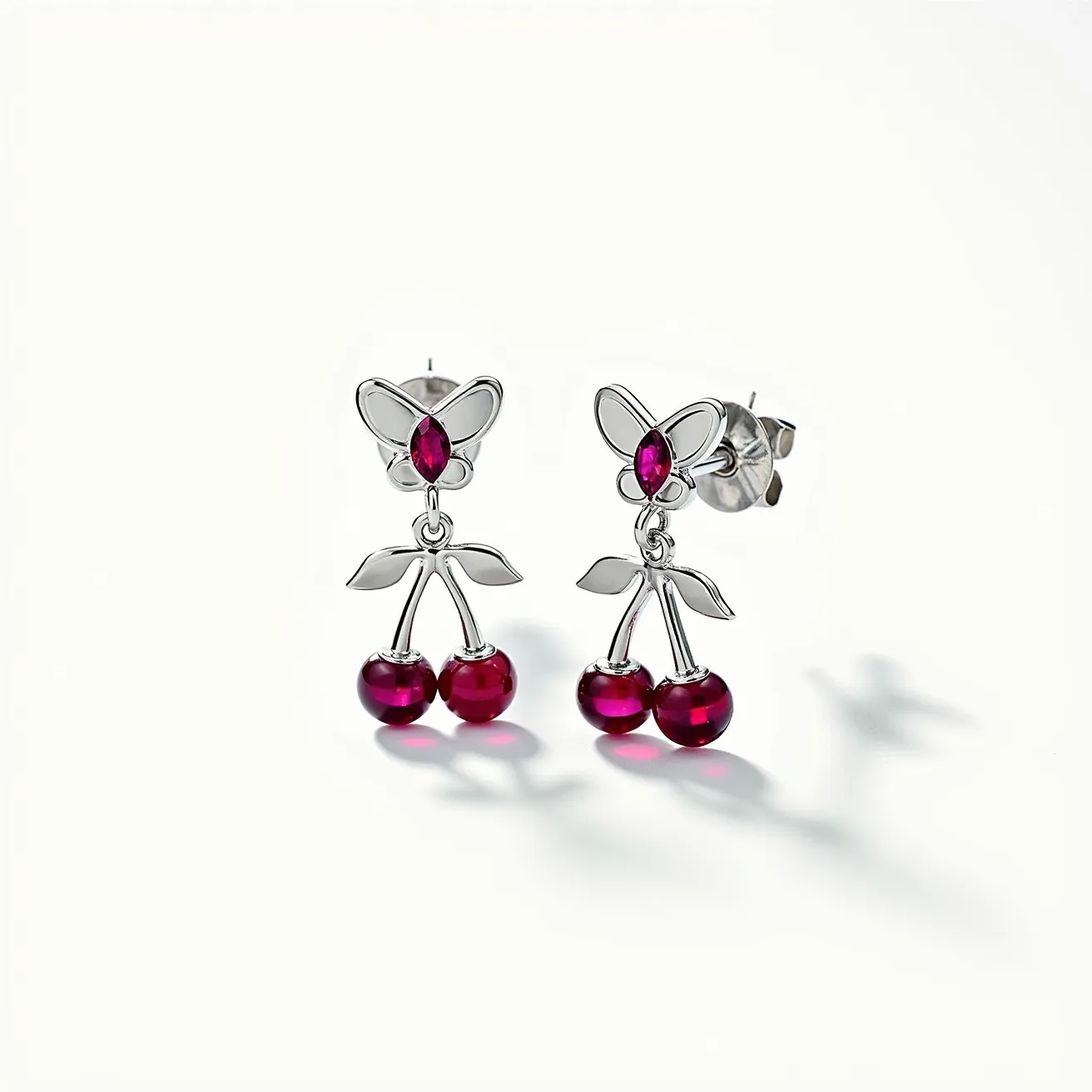 These cherry earrings feature a delightful cherry design with two round, glossy red beads that resemble cherries, likely made of a synthetic material or resin to mimic the look of stones. The stems and leaf accents appear to be crafted from a silver-toned metal, possibly stainless steel or sterling silver. At the top of each earring, a marquise-cut red gem, which might be a synthetic ruby or garnet, is prong-set, adding a touch of sparkle and elegance. The earrings utilize a butterfly or friction back clasp for secure and comfortable wear, making them both charming and practical accessories.