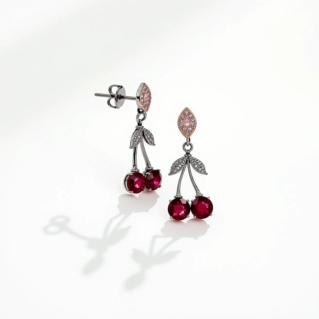 These cherry earrings feature a delightful design with vivid red gemstones forming the cherries, each cut in a round shape to enhance their brilliance. The stones are securely set in a metal setting that mimics the natural form of cherry stems and leaves. The leaves are intricately detailed and adorned with small clear stones that add a subtle sparkle. The earrings attach via a post and butterfly backing, ensuring a secure fit. Above the cherry design, a marquise-shaped setting holds a cluster of small pink stones, adding an elegant touch to the overall look. The combination of materials and colors beautifully captures the playful and fresh essence of cherries.