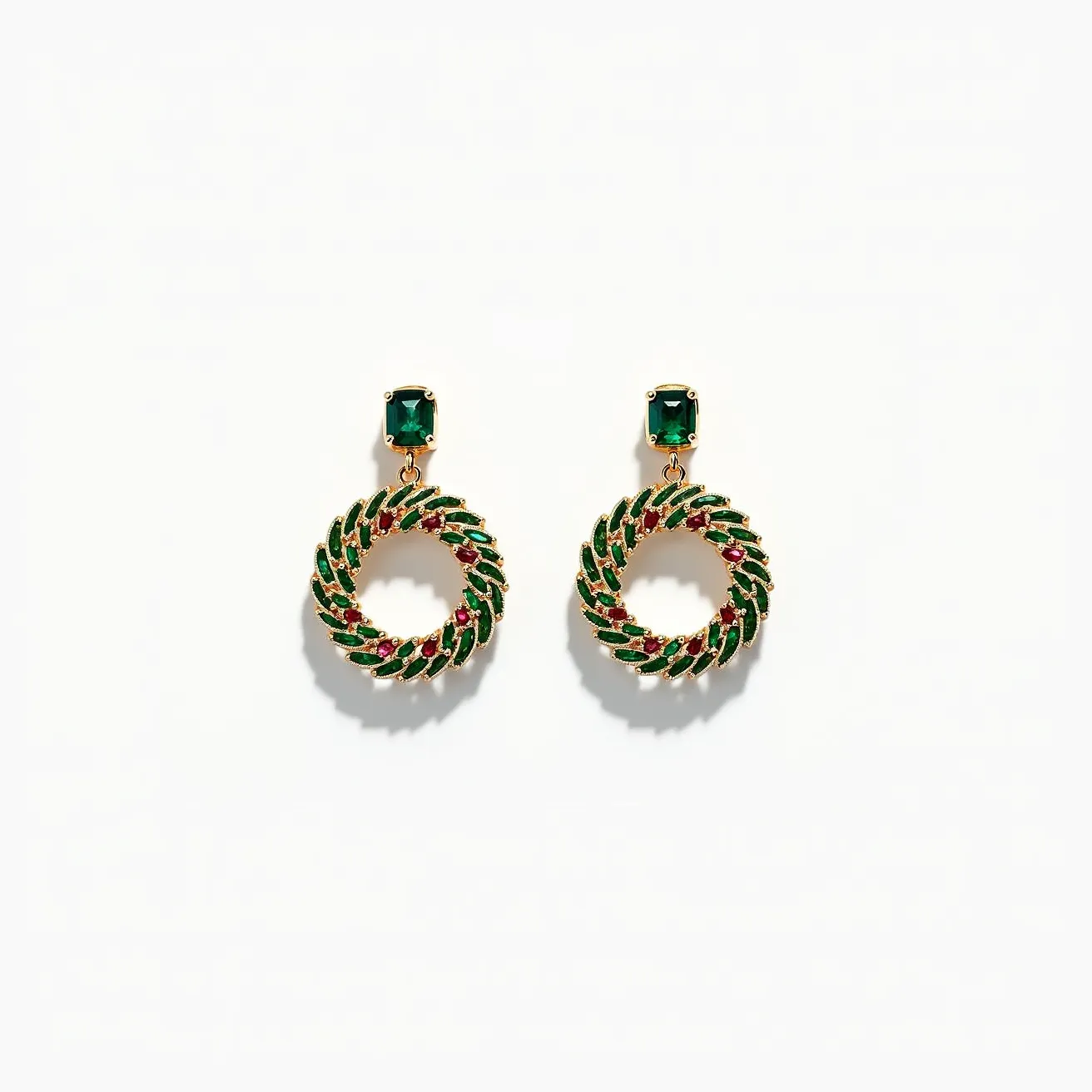 These Christmas earrings feature a festive design, showcasing circular wreaths embellished with alternating green and red stones. The green stones are likely enamel accents, while the red stones mimic berries, giving a traditional holiday aesthetic. Each earring is adorned with an emerald-cut green gem at the top, adding a touch of elegance. The earrings appear to have a gold-tone metal setting, which enhances the rich colors of the design. They are attached to the ear with a simple post and backing clasp, ensuring secure wear.