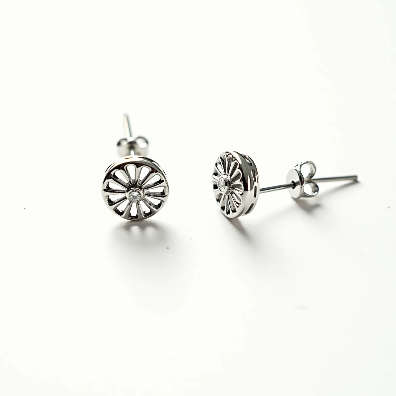 These circle earrings showcase a distinctive design made from a shiny metallic material, likely silver or white gold. At the center of each earring is a single, small, round gem that is clear and appears to be a diamond, set in a bezel-style setting. The earrings feature an intricate cut-out pattern resembling a floral motif, radiating outward from the center stone. The attachment mechanism is a simple post and butterfly clasp, ensuring a secure and classic fit for pierced ears.