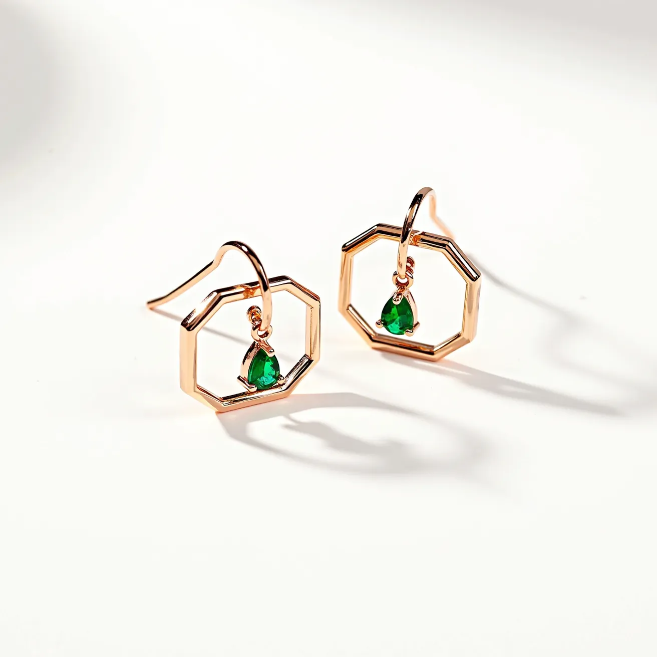 These circle earrings are elegantly crafted with a geometric octagonal shape, featuring a gold-toned metal as the primary material. Each earring is adorned with a vibrant green gemstone, cut in a teardrop shape and securely held in place with a discrete three-prong setting. The earrings are designed with a simple, curved hook clasp, allowing for easy and comfortable attachment. The combination of the gold tone and the green stone creates a striking and sophisticated aesthetic.