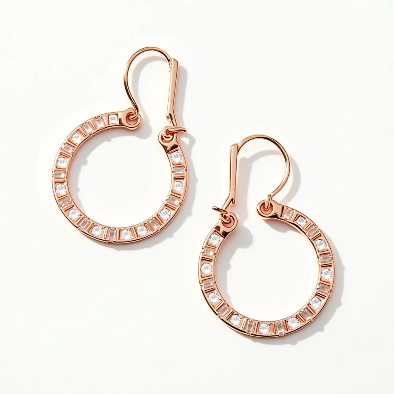 These circle earrings exhibit a refined design comprised of a likely rose gold metal that provides a warm, luxurious sheen. They are adorned with round-cut stones nestled within a series of bezel settings that evenly spaced around the circular frame, adding a consistent sparkle. The delicate design is complemented by a hook-style clasp that offers a seamless, secure attachment when worn. The craftsmanship highlights both simplicity and elegance, making these earrings versatile for a variety of occasions.