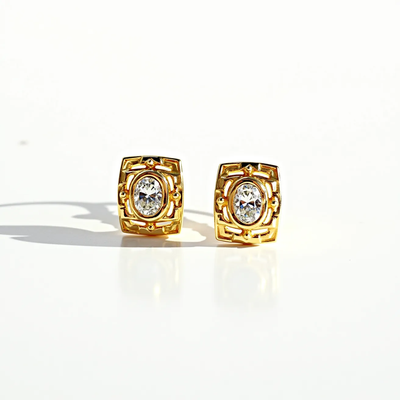 These clip on earrings feature a rectangular design crafted from a gold-toned metal. At the center of each earring is an oval-cut clear gemstone, likely a crystal or cubic zirconia, securely set in a bezel setting. The gold frame has an intricate, openwork pattern that adds a touch of elegance to the design. The clip-on mechanism allows for comfortable wear without the need for pierced ears.