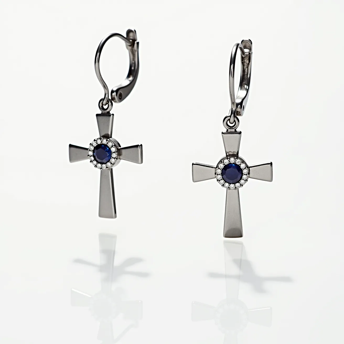 These cross earrings for men feature a sleek and polished metallic design, likely crafted from stainless steel or sterling silver, showcasing a bold and modern aesthetic. The centerpiece of each cross is adorned with a deep blue, round-cut gemstone, possibly a sapphire, surrounded by smaller clear stones, giving an elegant and refined touch through a halo setting. The earrings are attached using a lever-back clasp, ensuring both security and comfort for the wearer. The overall design combines a classic symbol with contemporary style, making it a versatile accessory for various outfits.