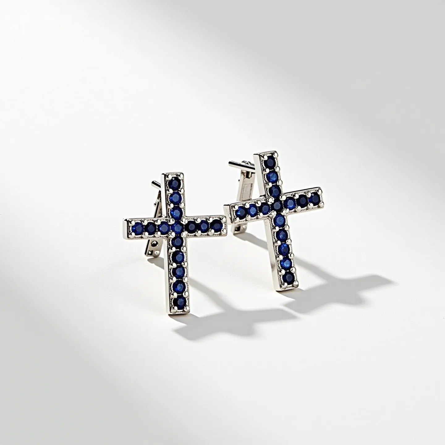 These cross earrings for women feature a design where each cross is adorned with circular, deep blue gemstones arranged in a linear fashion along the arms of the cross. The stones appear to be set in a polished metal, likely silver or white gold, which enhances the contrast with the vibrant blue hues of the gems. The earrings utilize a post and clutch back attachment, ensuring a secure fit when worn. The craftsmanship is highlighted by the neatly aligned gemstones, offering a striking and elegant accessory.