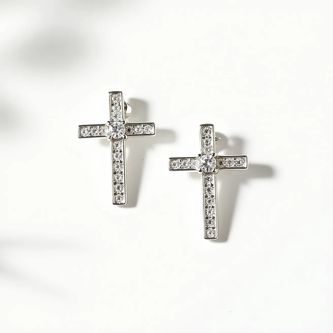 These cross earrings for women are crafted with a sleek, metallic material, likely silver or white gold, forming a classic cross shape. Each arm of the cross is adorned with small, round-cut clear stones, possibly diamonds or cubic zirconia, set in a pave style that enhances their sparkle. At the center of each cross, there is a larger, prominent round-cut stone, securely set to catch the light and add to the earrings' elegance. The earrings appear to have a post-back attachment, ensuring a secure and comfortable fit for pierced ears.