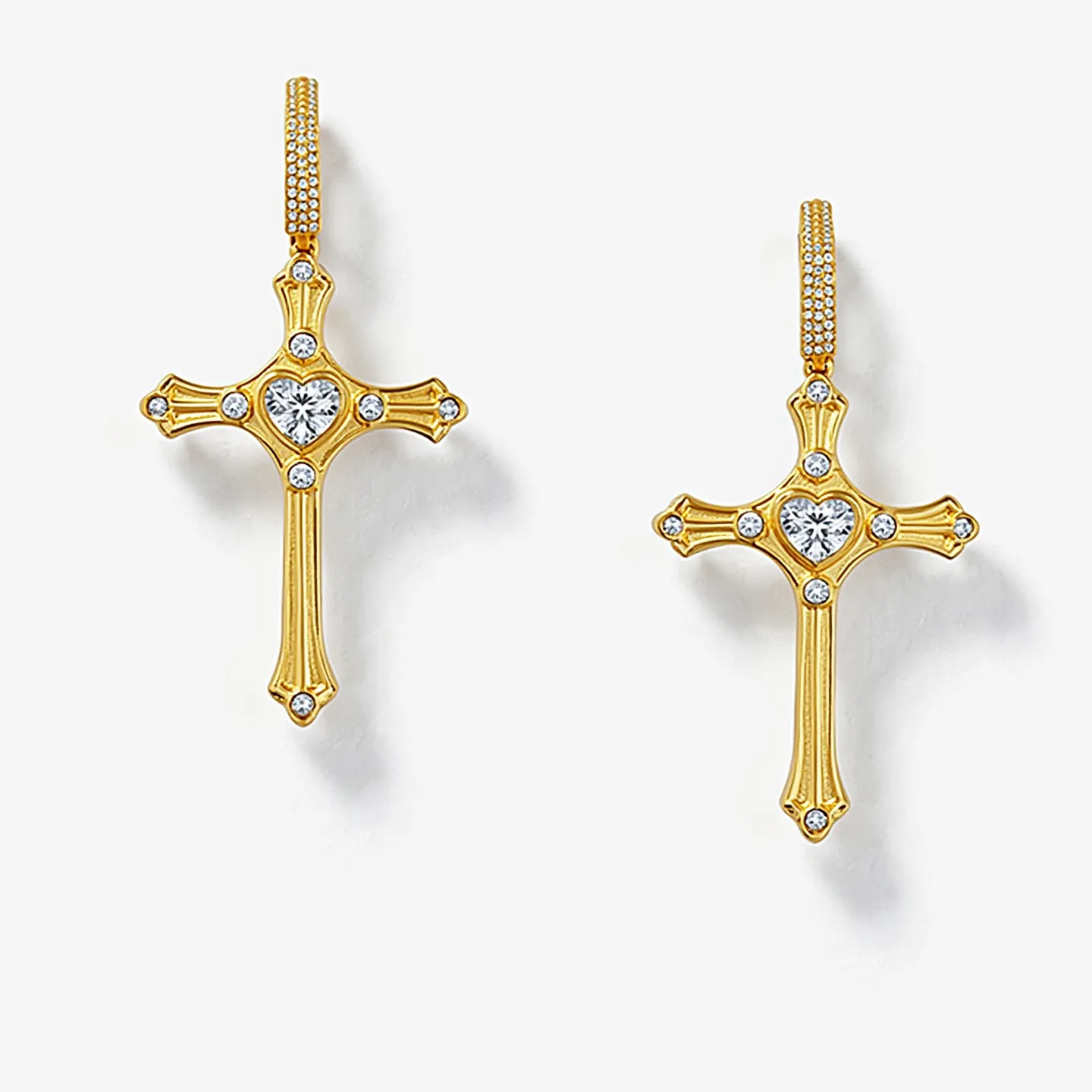 These cross earrings for women are elegantly crafted from gold-toned metal, featuring a detailed design that prominently includes sparkling clear gemstones. Each arm of the cross is adorned with small round cut gems, complementing the larger heart-shaped gemstone centrally set, drawing attention to its brilliance. The hoops attached to the crosses are embellished with an array of tiny round gems, enhancing their shimmer. The earrings likely use a hinged closure or lever back for secure attachment, ensuring they stay in place elegantly. The combination of intricate detailing and the radiant gems creates a striking, sophisticated accessory.