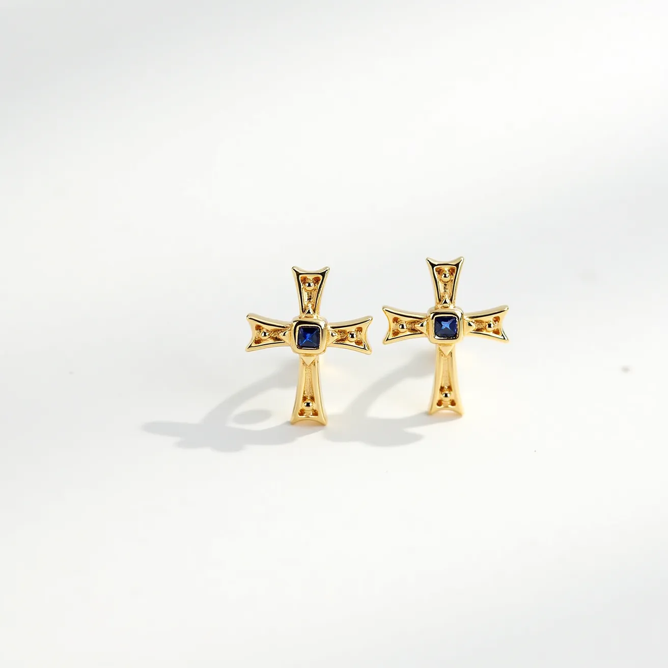 These cross earrings for women feature a distinct design crafted from gold-toned metal, forming a traditional cross shape. Each earring is embellished with a single square-cut blue gemstone centrally set, accentuating the elegance and providing a striking contrast against the golden hue. The stones are securely held in a bezel setting, which enhances their prominence while ensuring durability. These earrings adopt a stud style for attachment, providing a simple and secure fit for the wearer.