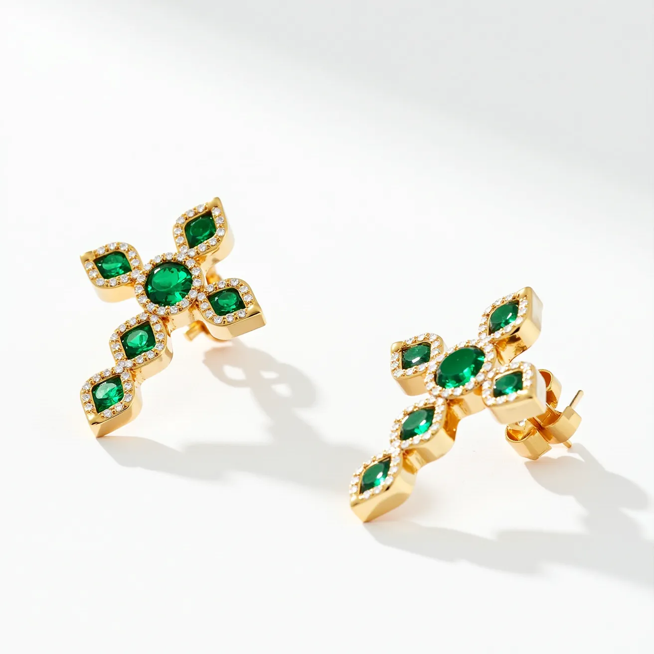 These cross earrings for women feature a striking design made of gold-tone metal. They are adorned with vibrant green, oval-cut gems set in the center and surrounded by smaller clear stones that form the cross's outline. The gems are held in prong settings, enhancing their visibility and brilliance. The earrings are secured with a post-back clasp, providing a secure and comfortable fit for the wearer. The combination of the rich green and the gold-tone metal creates a luxurious and elegant aesthetic.