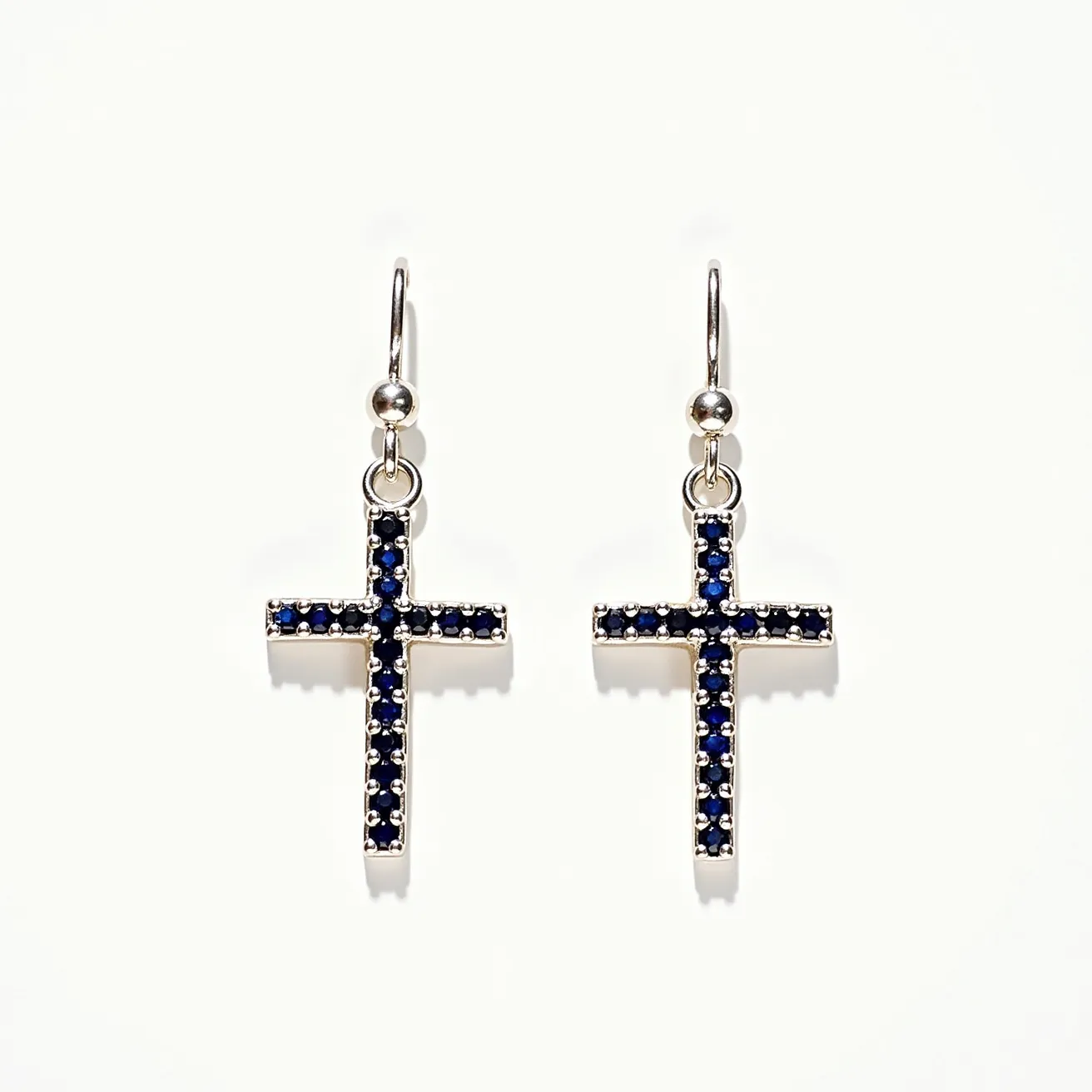 These cross earrings for women feature a classic cross design adorned with dark blue stones that appear to be small round-cut sapphires. The stones are securely set in a pronged setting, adding a touch of elegance and allowing light to highlight their rich color. The crosses are attached to a fine metal loop, likely silver or a similar shiny metal, which leads to a hook clasp, offering a secure yet easy-to-use attachment method. The overall design exudes a blend of simplicity and sophistication, making them versatile for various occasions.