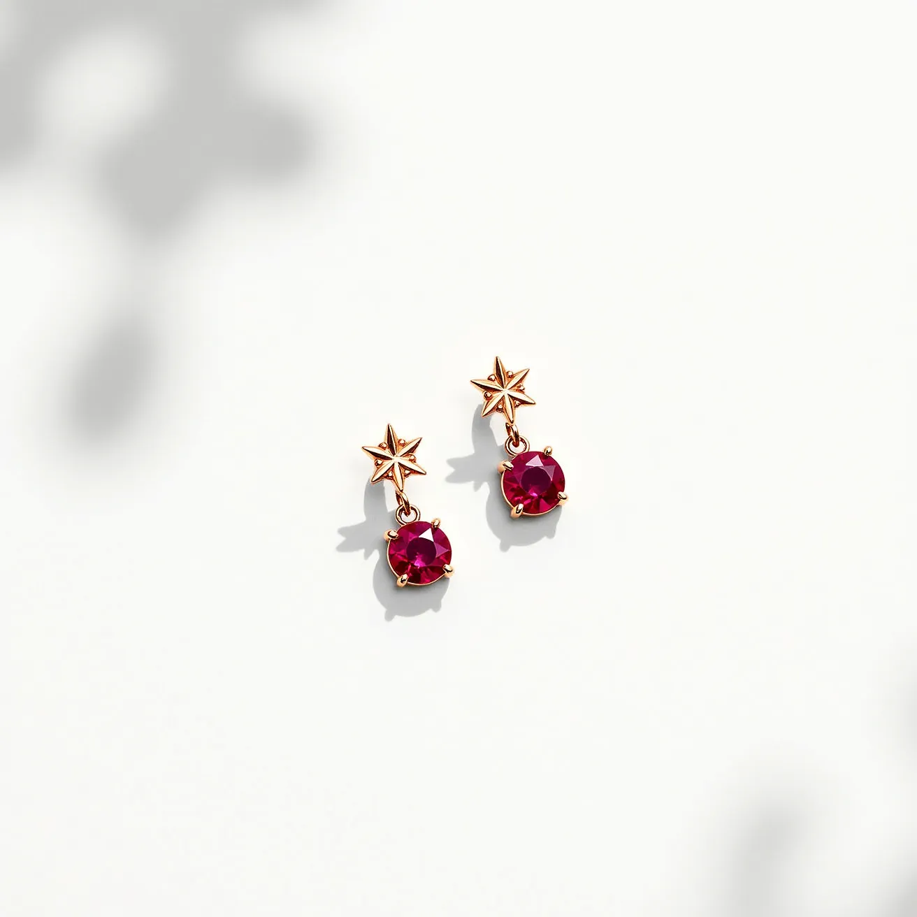 These dangle earrings feature a star-shaped design with a gold color setting. Each earring is adorned with a round, faceted red gemstone, likely set in a four-prong style that accentuates its brilliance. The earrings dangle elegantly from a small loop beneath the star, providing movement and sparkle. The star and gemstone combination creates a celestial theme. The attachment mechanism appears to be a post, suitable for pierced ears, offering a secure fit while allowing the design to dangle freely.