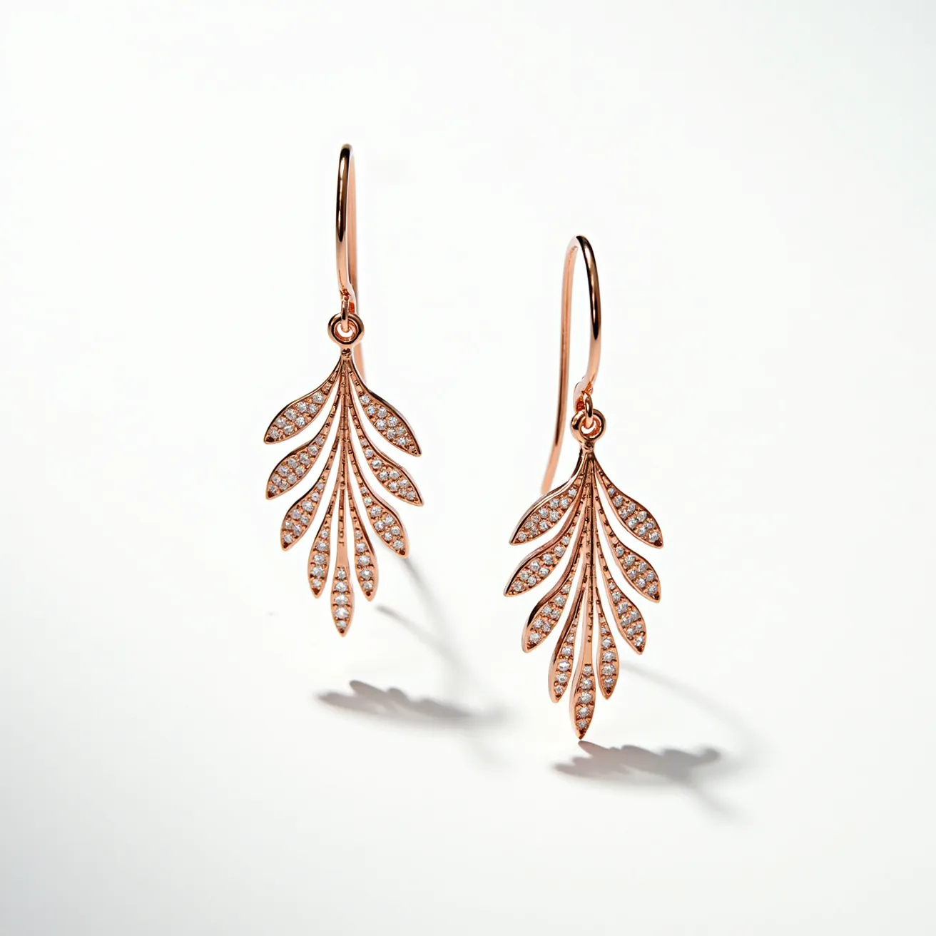 These dangle earrings showcase a delicate design crafted from rose gold, featuring an elegant leaf-like motif. Each leaf segment is embellished with small, round-cut white gemstones that sparkle against the metal, likely set in a pavé style, enhancing the overall radiance of the design. The earrings are attached to simple hook clasps, allowing them to dangle freely and catch the light with movement. The intricate detailing and the combination of materials create a sophisticated and charming accessory.