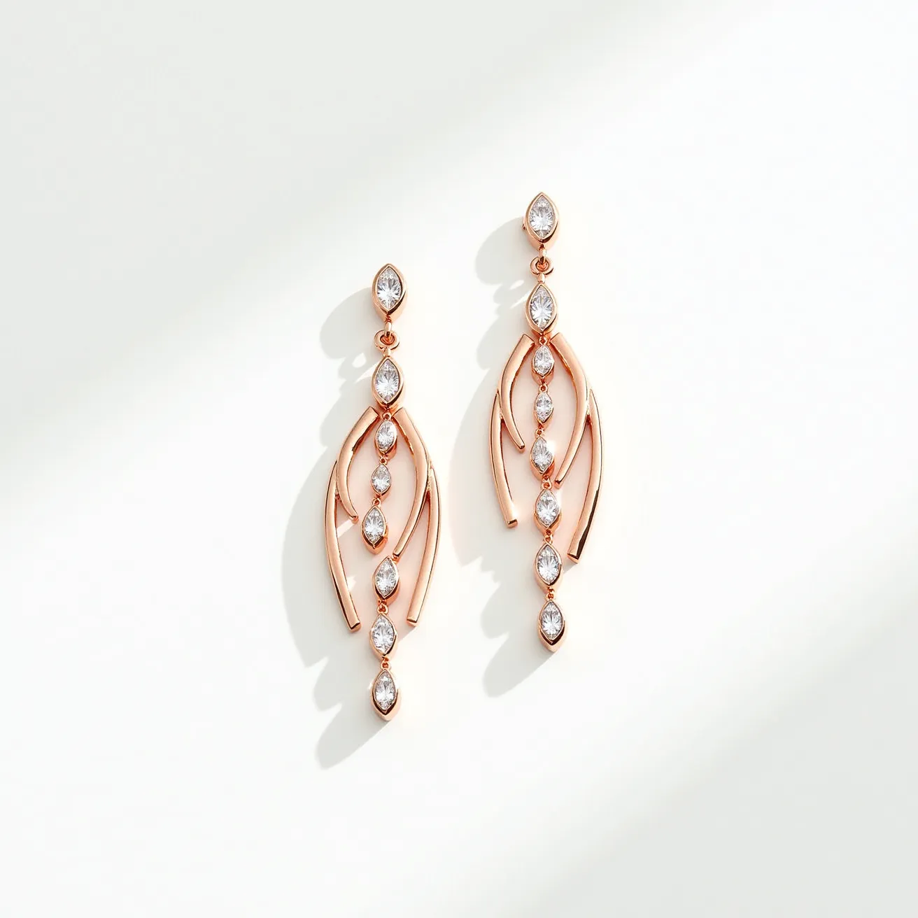 These dangle earrings feature a graceful blend of rose gold-toned metal with a series of marquise and round-cut transparent stones, likely cubic zirconia or diamonds, set intricately along the central lines. The stones are positioned in bezel settings, providing an elegant shine and security. The earrings are arranged with a delicate, flowing design, incorporating curved metal elements that amplify the sparkle of the stones. The attachment mechanism appears to be a post and friction back, ensuring ease of wear and a secure fit. The overall design exudes a sophisticated and modern look, perfect for adding elegance to any ensemble.