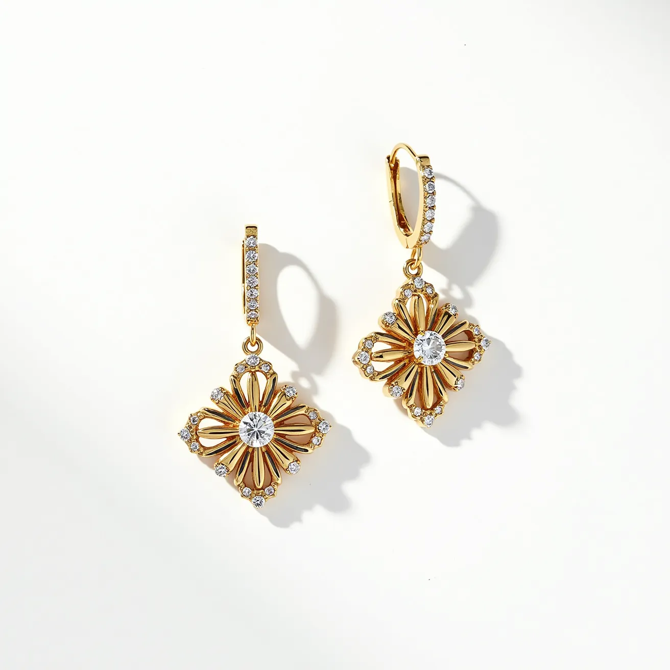 These dangle earrings feature an intricate floral design crafted from gold-toned metal. At the center of each earring is a round, brilliant-cut gem set within a starburst pattern. Surrounding the central gem are smaller, similarly cut stones embedded in a delicate pave setting, adding sparkle and elegance. The earrings attach with a secure lever-back clasp, which is also adorned with additional stones, enhancing the cohesive, dazzling appearance of the piece. The combination of these elements creates a timeless and sophisticated look, perfect for formal occasions.