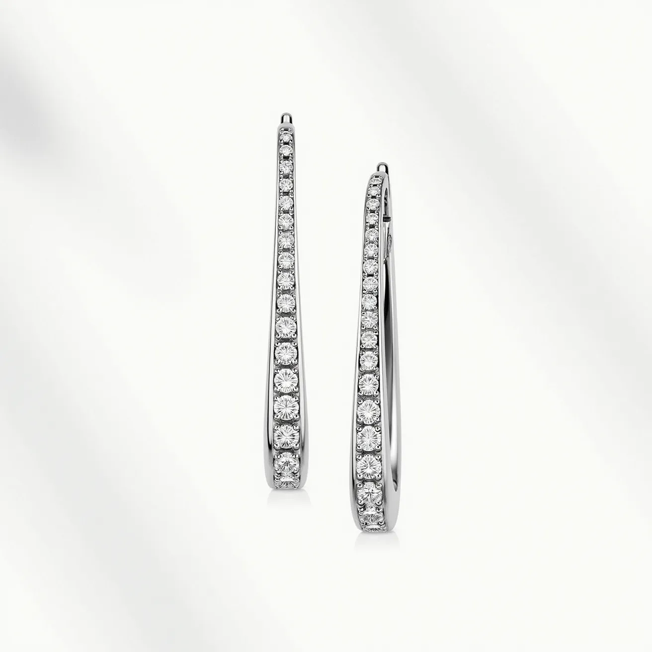 These diamond earrings showcase a sleek and elegant design, featuring a series of round-cut diamonds that are meticulously set in a linear pattern along the entire length of each earring. The diamonds are likely mounted in a secure and precise channel setting, allowing the light to enhance their brilliance. The body of the earrings is crafted from a shiny, reflective metal, possibly white gold or platinum, which complements the shimmer of the diamonds. These earrings employ a hook or wire clasp mechanism, lending a seamless and graceful form that allows for easy wear. The overall design emphasizes sophistication and timeless beauty, making them a striking accessory.