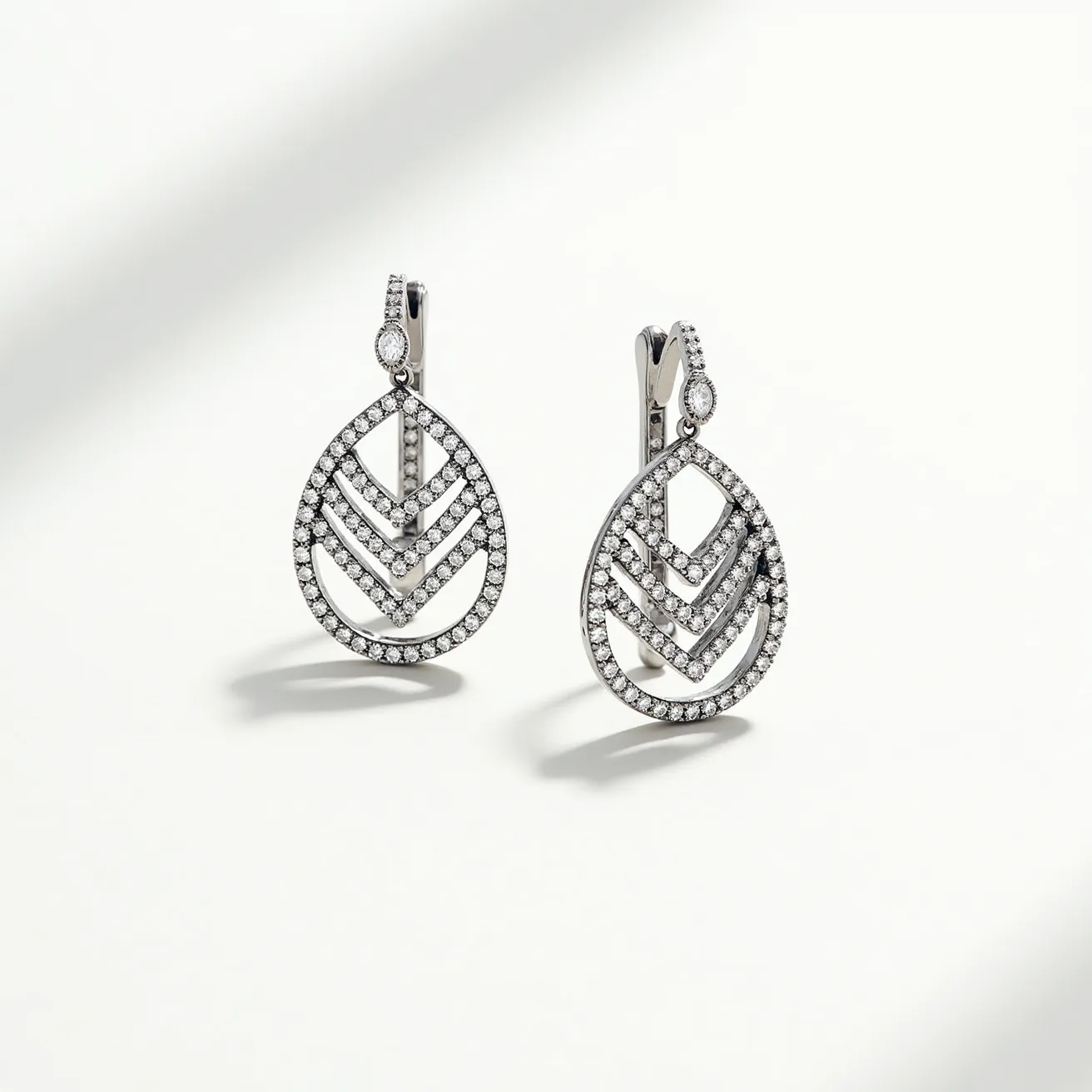 These diamond earrings feature an elegant teardrop design, crafted with a series of interlocking chevron patterns encrusted with small round-cut diamonds. The setting is likely made from a polished white metal, possibly white gold or platinum, which accentuates the brilliance of the stones. At the top of each earring, a small oval-shaped diamond is set vertically, adding a touch of refinement. The earrings are secured with lever-back clasps, providing both a secure fit and ease of wear.