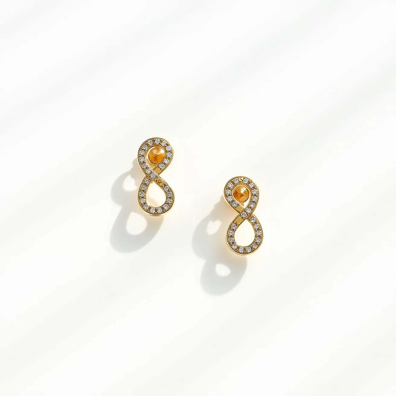 These diamond earrings feature an elegant infinity design crafted from a gold metal. The earrings are adorned with small, round-cut diamonds set along the outer loops, enhancing their shimmering appearance. At the center of each earring, a vibrant, round yellow gem adds a pop of color, possibly a citrine or similar stone. The earrings likely use a post or similar attachment at the back for secure wear, complementing their refined, luxurious look.