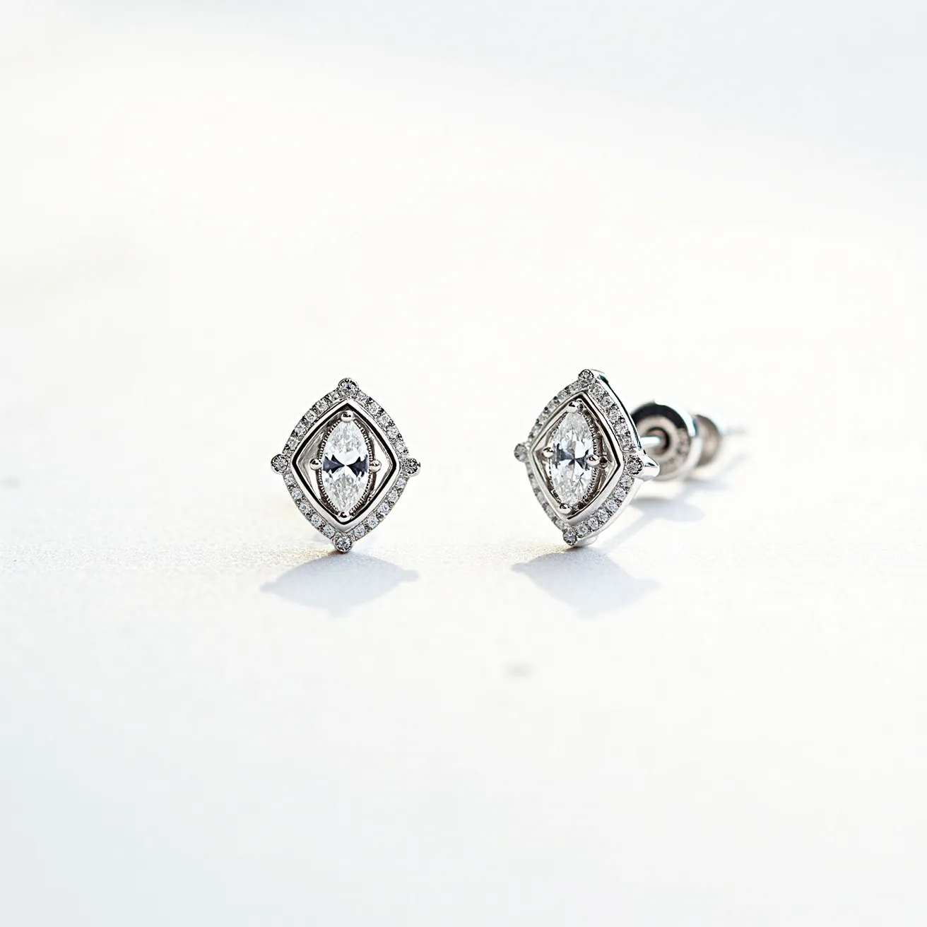 These diamond earrings feature a stunning marquise-cut diamond at their center, set within a sleek, white metal, likely platinum or white gold, that accentuates the brilliance of the gem. The central diamond is encircled by a halo of smaller round-cut diamonds, adding an extra layer of shimmer and sophistication. The setting is a four-prong arrangement for the central stone, ensuring security and stability. The earrings employ a classic post and butterfly back closure, providing a secure and comfortable fit for the wearer. The overall design showcases an elegant interplay of geometric shapes, enhancing the earrings' contemporary aesthetic.