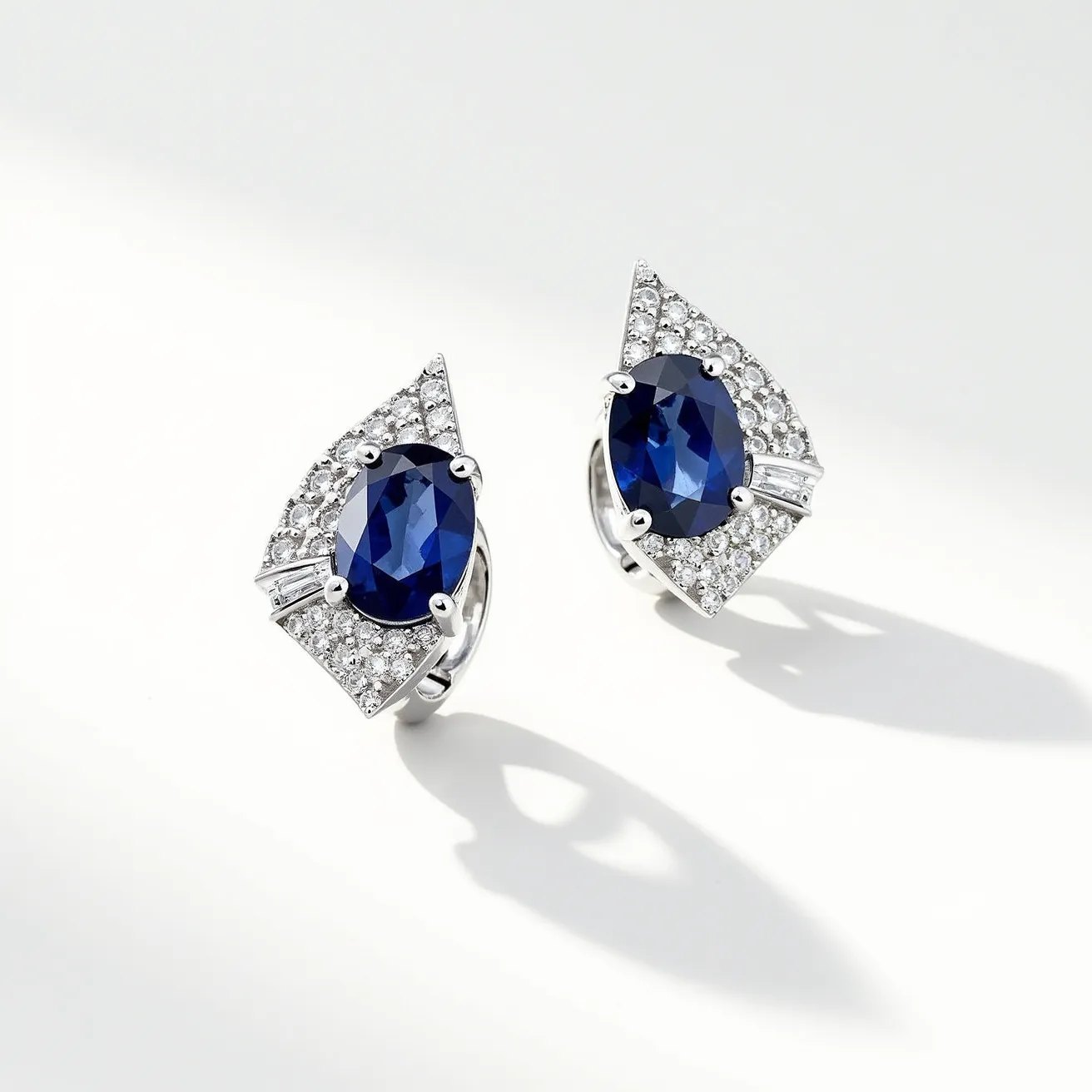 These diamond earrings feature an exquisite design centered around an oval-cut blue sapphire as the main gemstone. The sapphires are elegantly set in a secure prong setting, allowing the deep blue hues to be prominently displayed. Surrounding the sapphires are pavé set diamonds that add a brilliant sparkle, complementing the central stone beautifully. The earrings are crafted from a polished white metal, likely white gold or platinum, which enhances the overall sophistication of the piece. The earrings are finished with a clip or hinged back clasp, ensuring both security and comfort when worn.