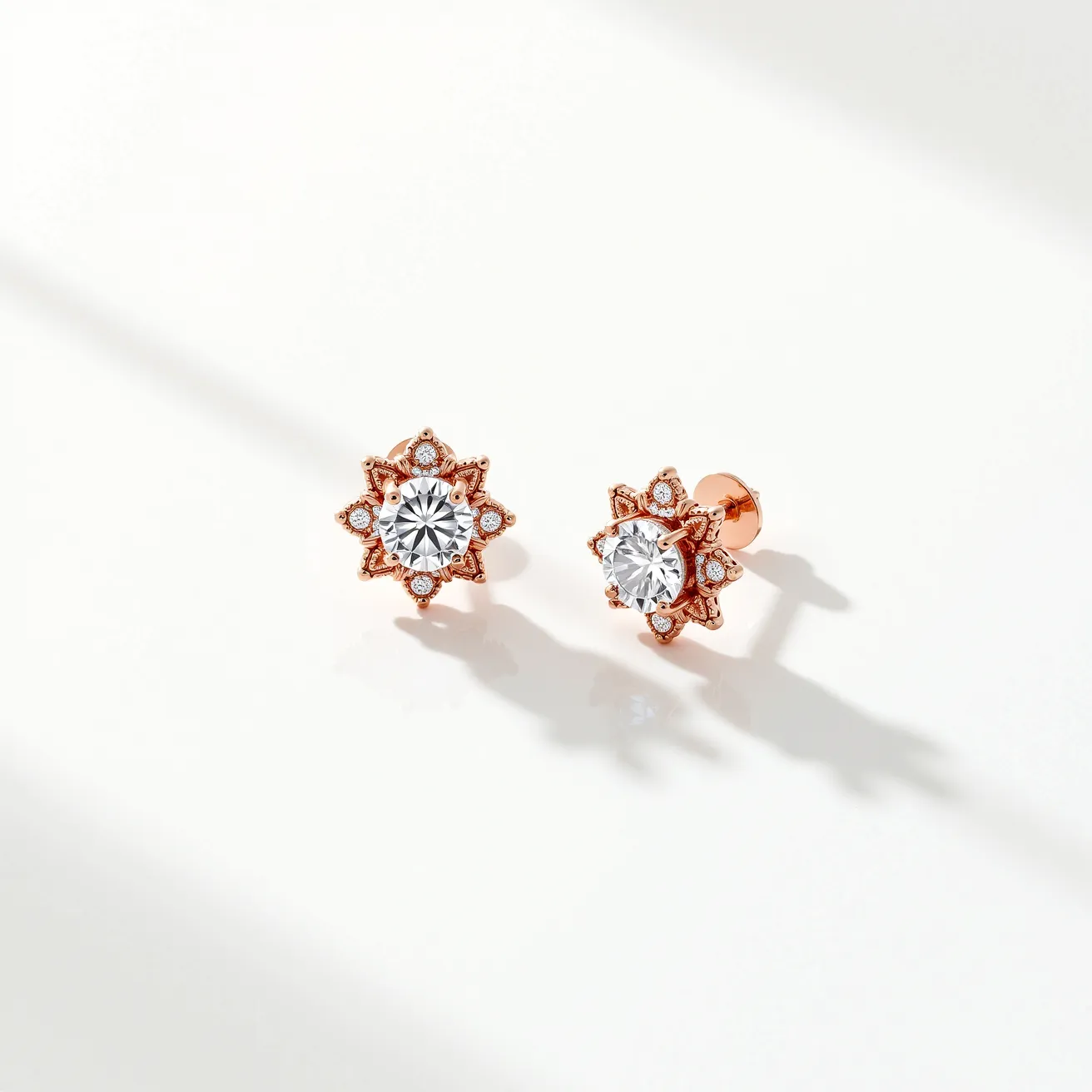 These diamond earrings feature a central round-cut diamond set prominently in a starburst design. The main diamond is surrounded by smaller round diamonds, enhancing the intricate pattern. The setting appears to be crafted in a warm, rose gold metal, contributing to the earrings' elegant and luxurious appearance. The earrings are secured with a push-back clasp, ensuring they stay comfortably in place. The combination of the central stone and detailed setting creates a striking, sophisticated look.