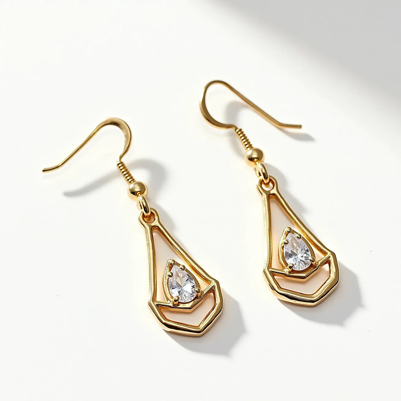 These drop earrings feature a modern, geometric design crafted from a gold-toned metal. Each earring showcases a singular pear-cut clear stone, likely a cubic zirconia or similar gem, which is prong-set at the center of the design. The stone is framed by an open, abstract teardrop outline, which adds to the overall elegance and sophistication. The earrings are attached with a classic fish hook clasp, offering easy wearability and a stylish finish.