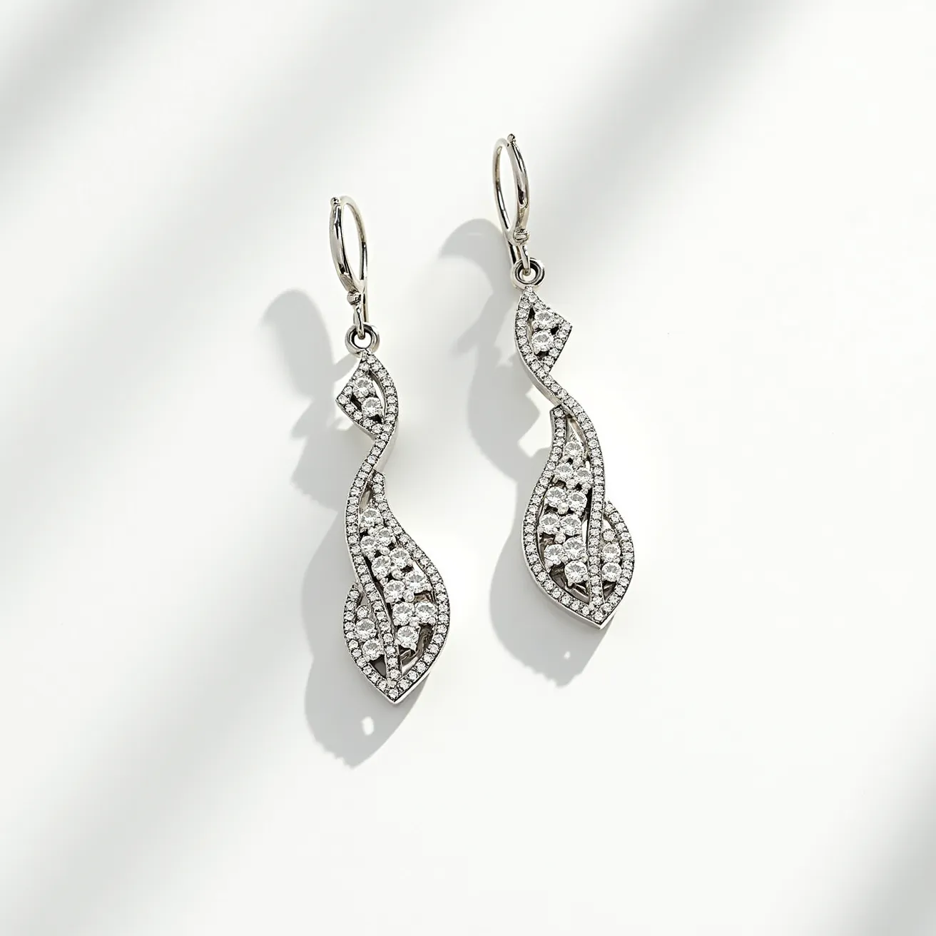 These drop earrings feature an elegant, flowing design crafted from a silver-toned metal, giving them a sleek and modern appearance. The earrings are adorned with numerous small, round-cut clear stones, likely diamonds or diamond simulants, set in a pave arrangement that enhances their sparkle and creates a shimmering effect. The stones are securely set in a way that follows the gentle, wave-like curves of the design, adding a contemporary twist to their classic glamor. The earrings are attached using lever-back clasps, ensuring a secure and comfortable fit for the wearer. The meticulous placement of the stones and the fluid shape make these earrings a stunning accessory suitable for both formal and casual occasions.